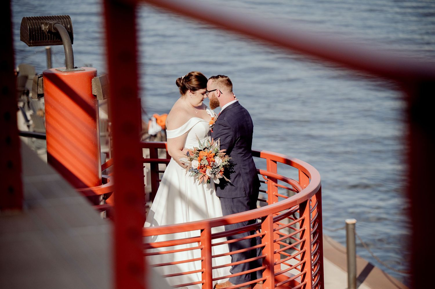 Pier B Duluth Wedding A couple sharing a romantic moment on an orange-railed deck overlooking the water.