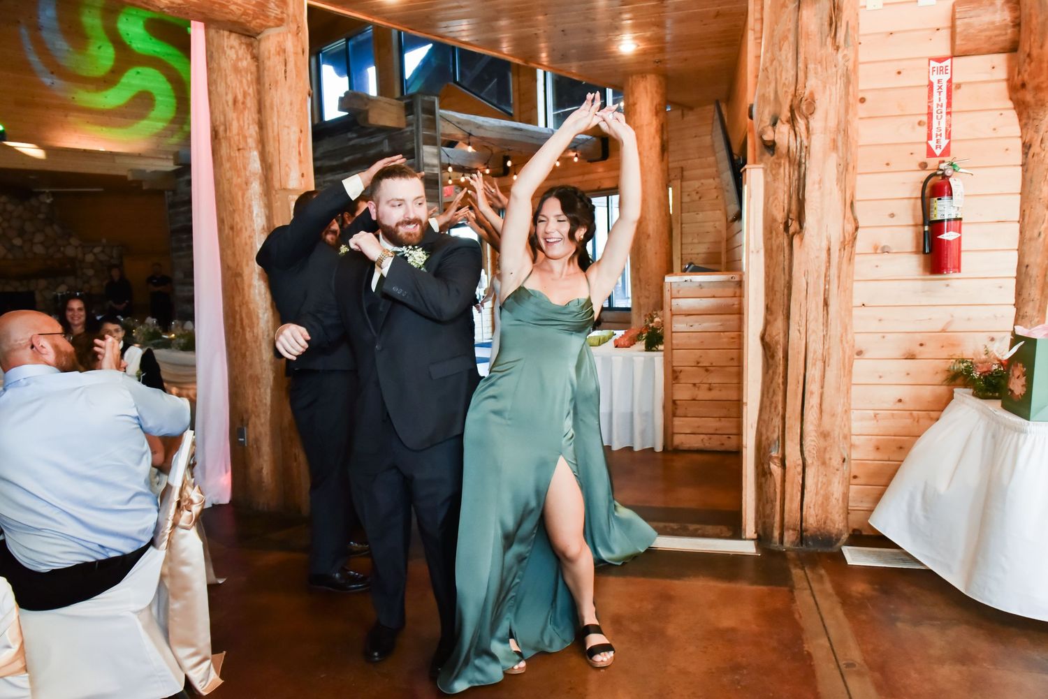 Wedding reception guests dancing and celebrating in a rustic wooden venue with string lights overhead.