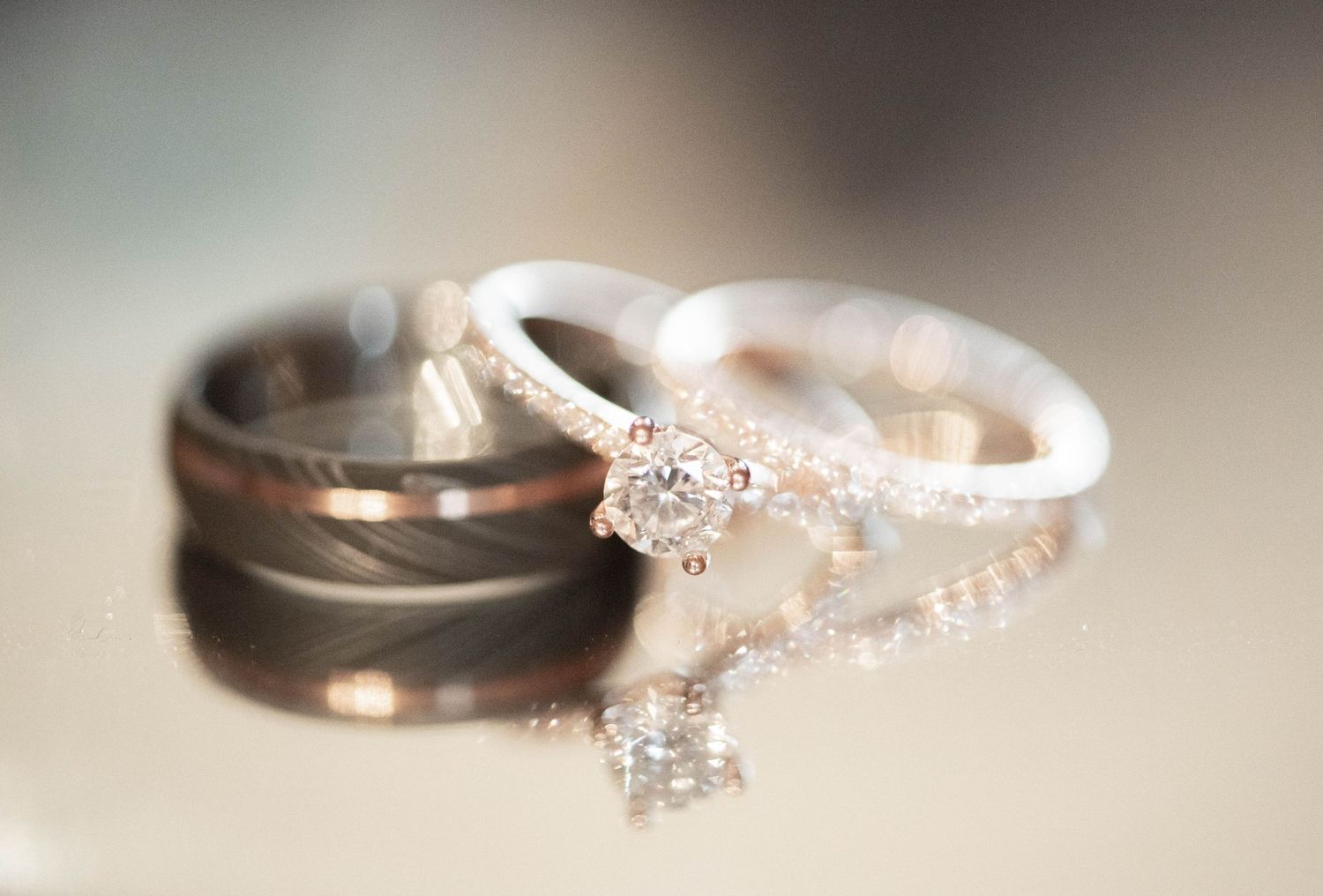 Wedding rings with one diamond engagement ring and one brushed metal band photographed in soft focus.