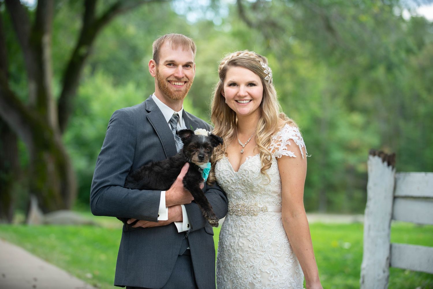A couple in wedding attire poses with their small black dog wearing a bowtie collar. Rum River Barn Milaca Minnesota Weddings