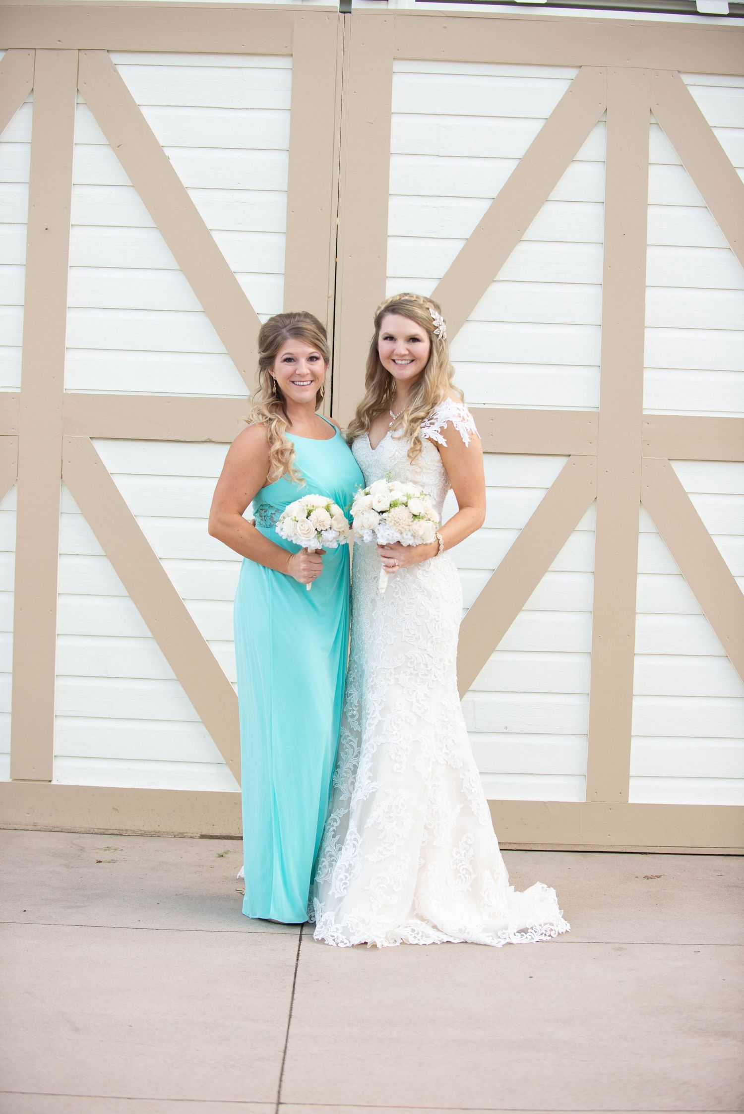 Two women pose together against barn doors, one wearing turquoise and one in a white lace wedding gown. Milaca Minnesota Weddings