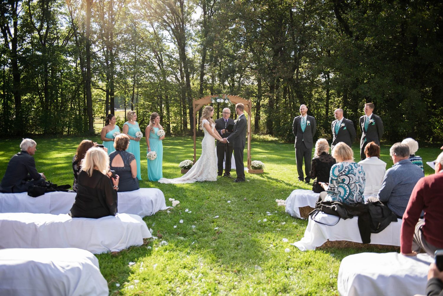 Wedding guests seated outdoors on white chairs in a lush garden setting during a ceremony. Rum River Barn Milaca Minnesota Weddings