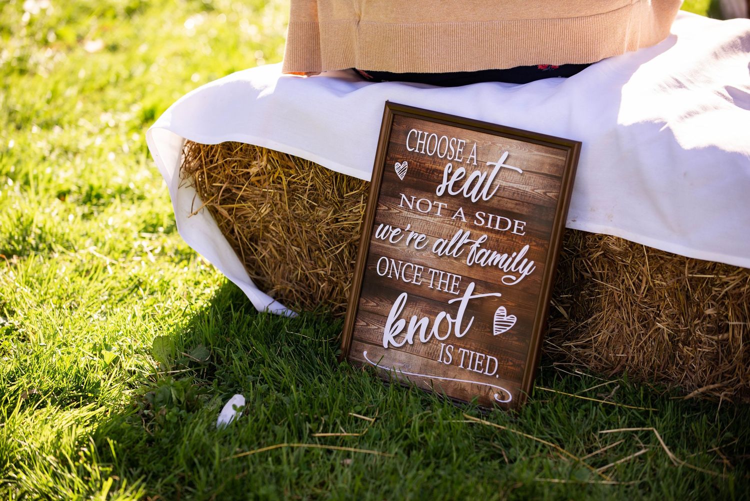 Rustic wooden wedding sign placed against hay bale with text about tying the knot. Rum River Barn Milaca Minnesota Weddings