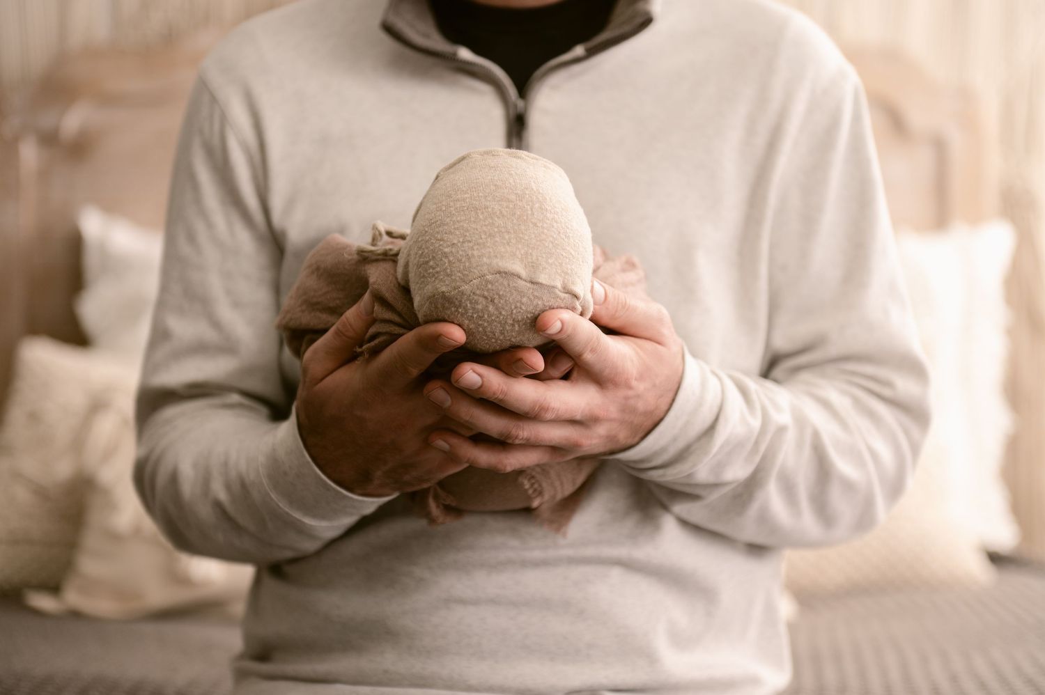 Person in white sweater holding small round knit object against soft neutral background.