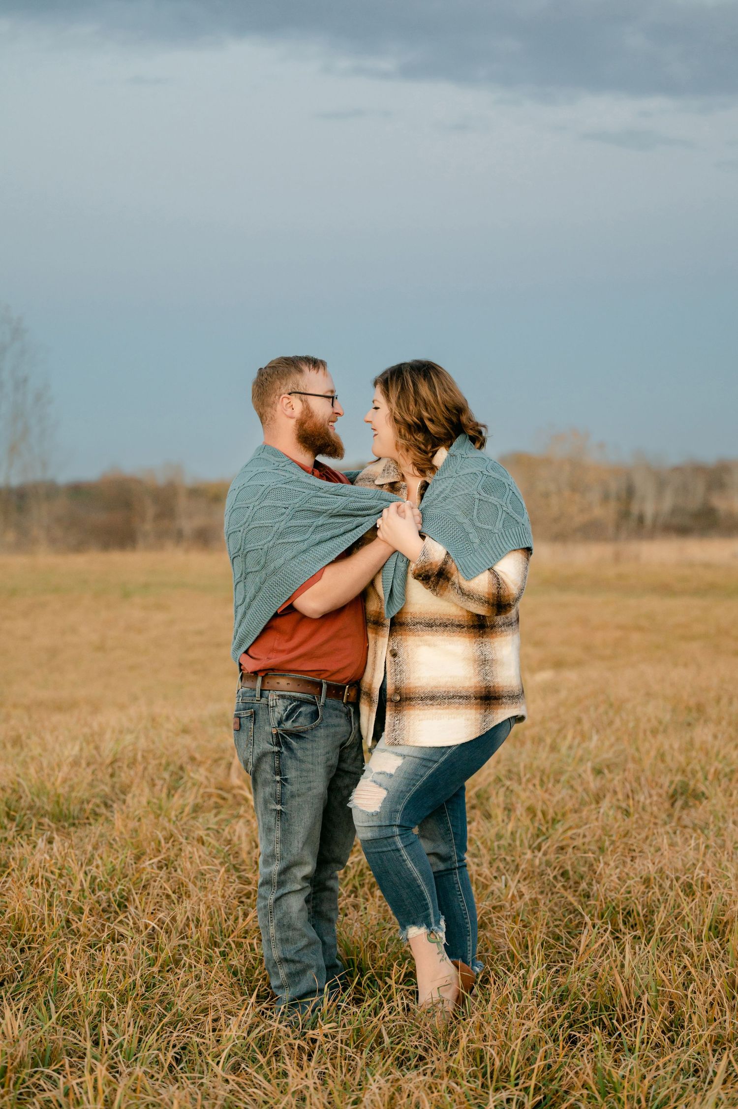 Loving couple embracing and laughing together in a rustic field during golden hour photoshoot.