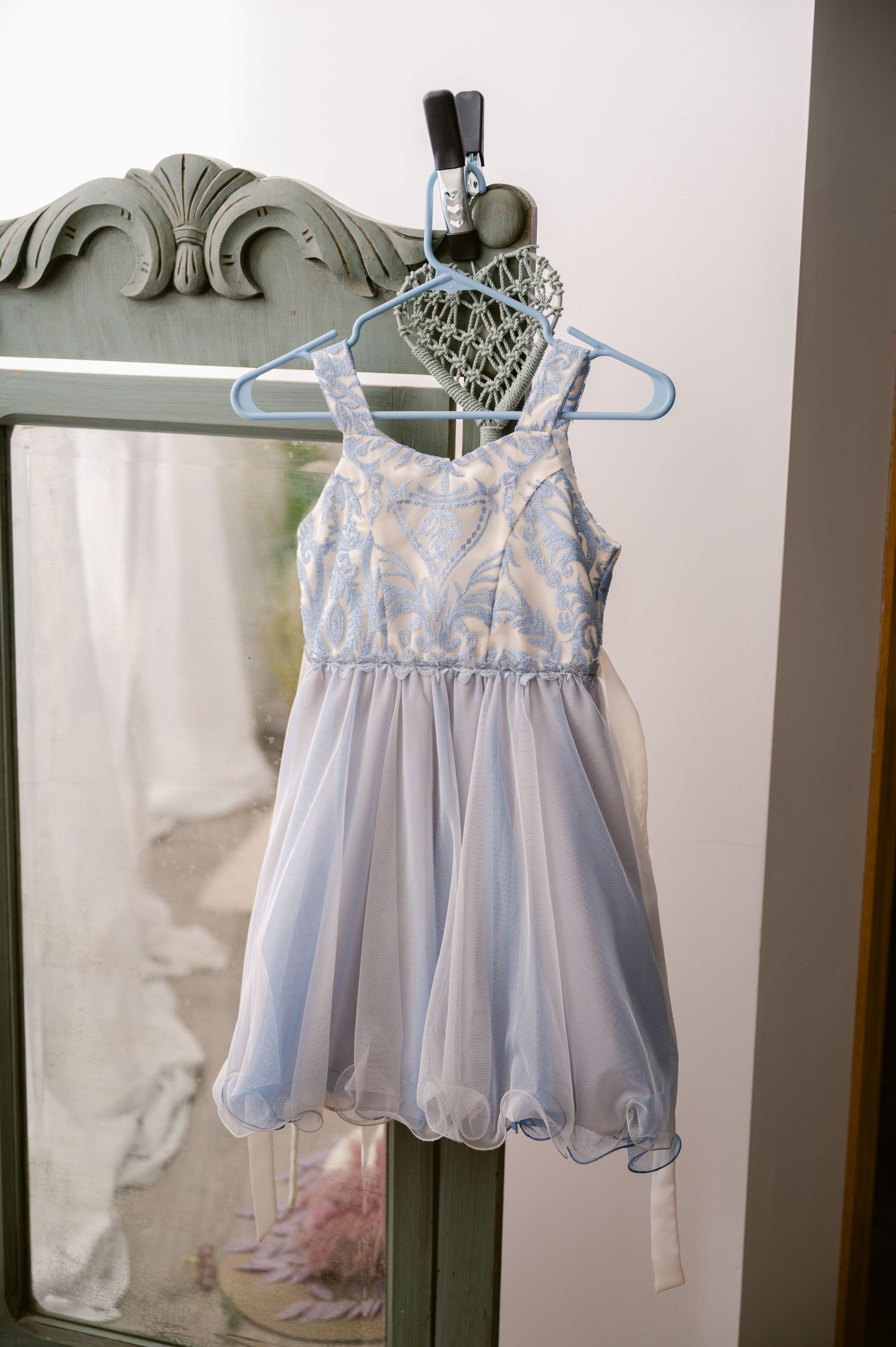 Light blue tulle party dress for a child hangs on a hanger with a decorative heart against a mirror or wall.