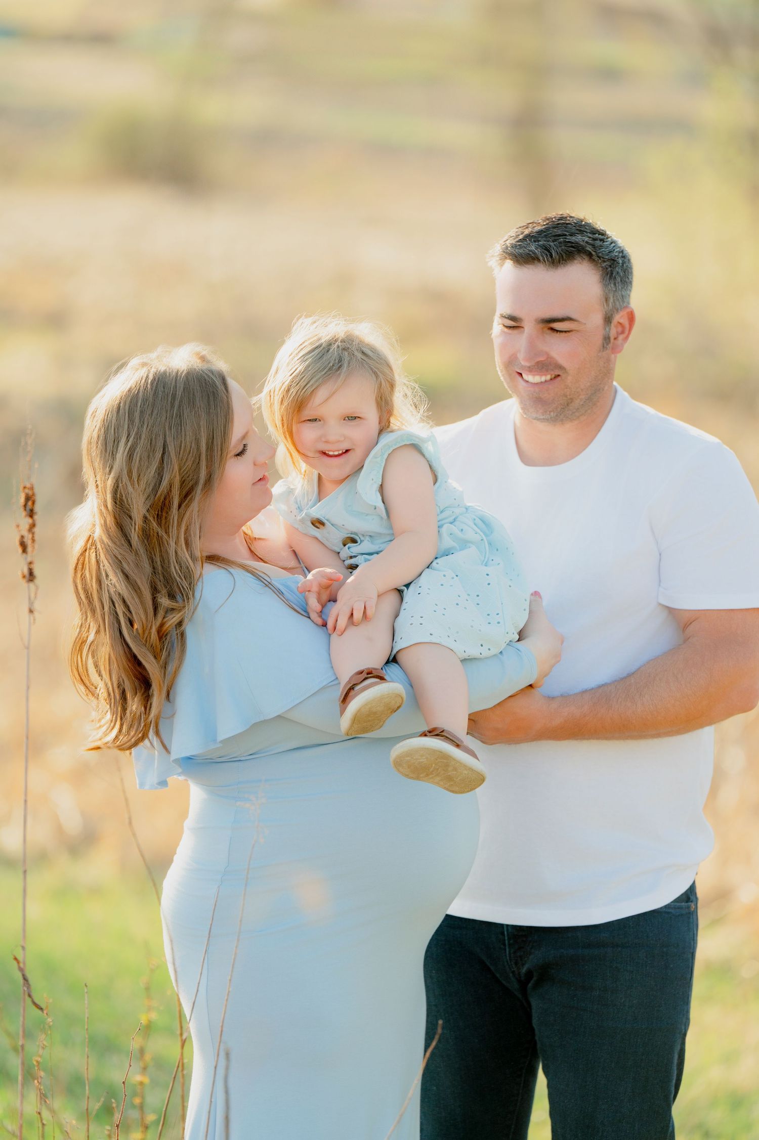 Family poses together in outdoor setting during golden hour maternity photoshoot.