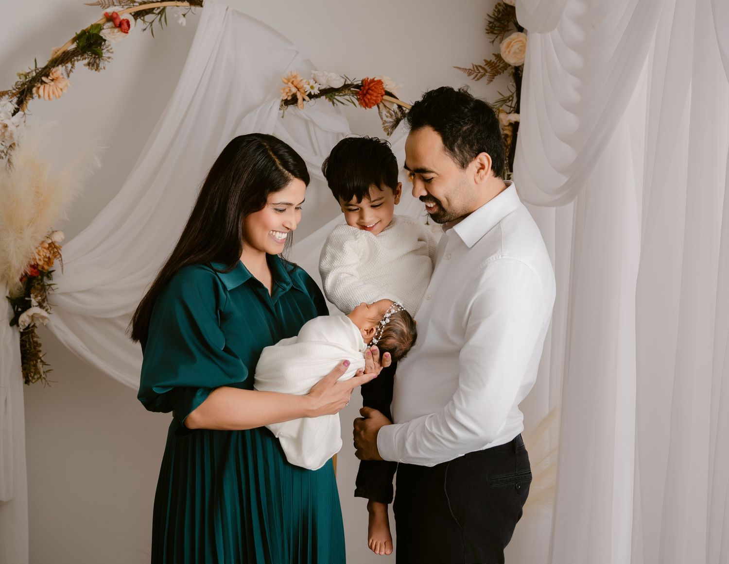 Intimate family portrait against white draped backdrop with floral garland decoration.