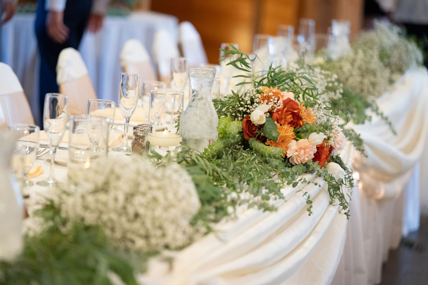 The Grands At Mulligans. Elegant wedding reception head table with white linens, floral arrangements, and baby's breath decorations.