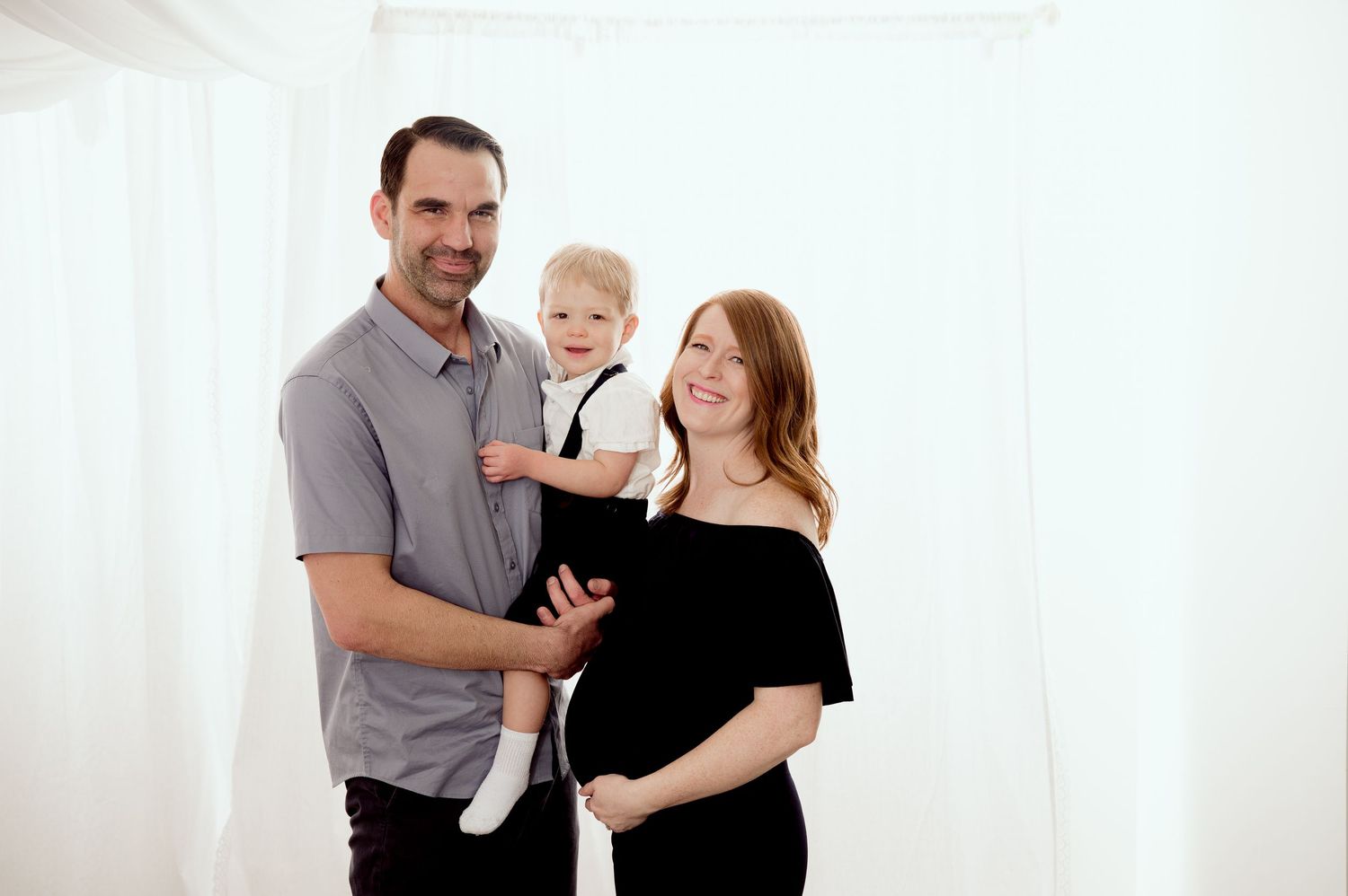 Three people pose together against a white backdrop during an indoor family photo session.