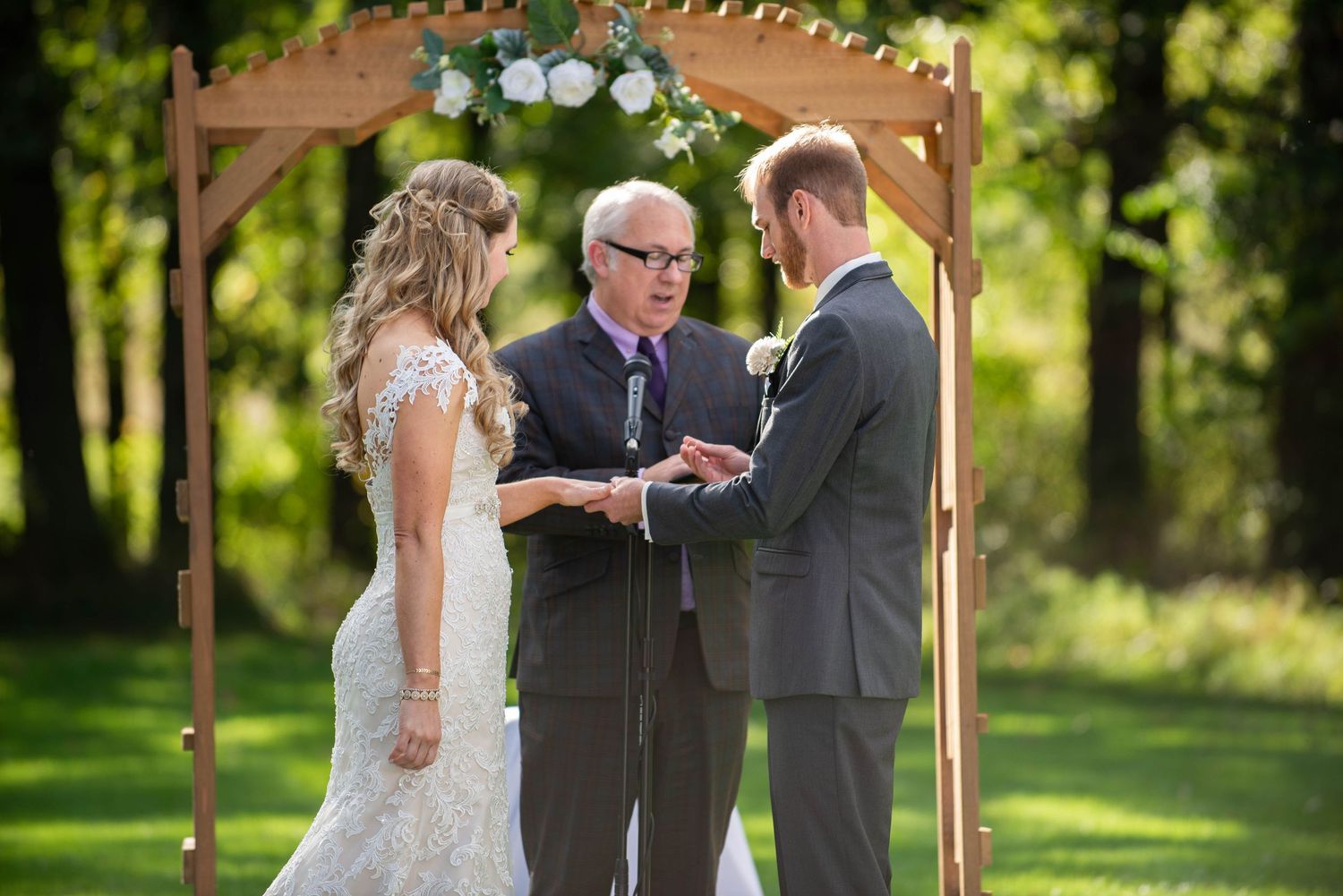 Wedding ceremony under wooden arch with floral decorations in garden setting. Rum River Barn Milaca Minnesota Weddings