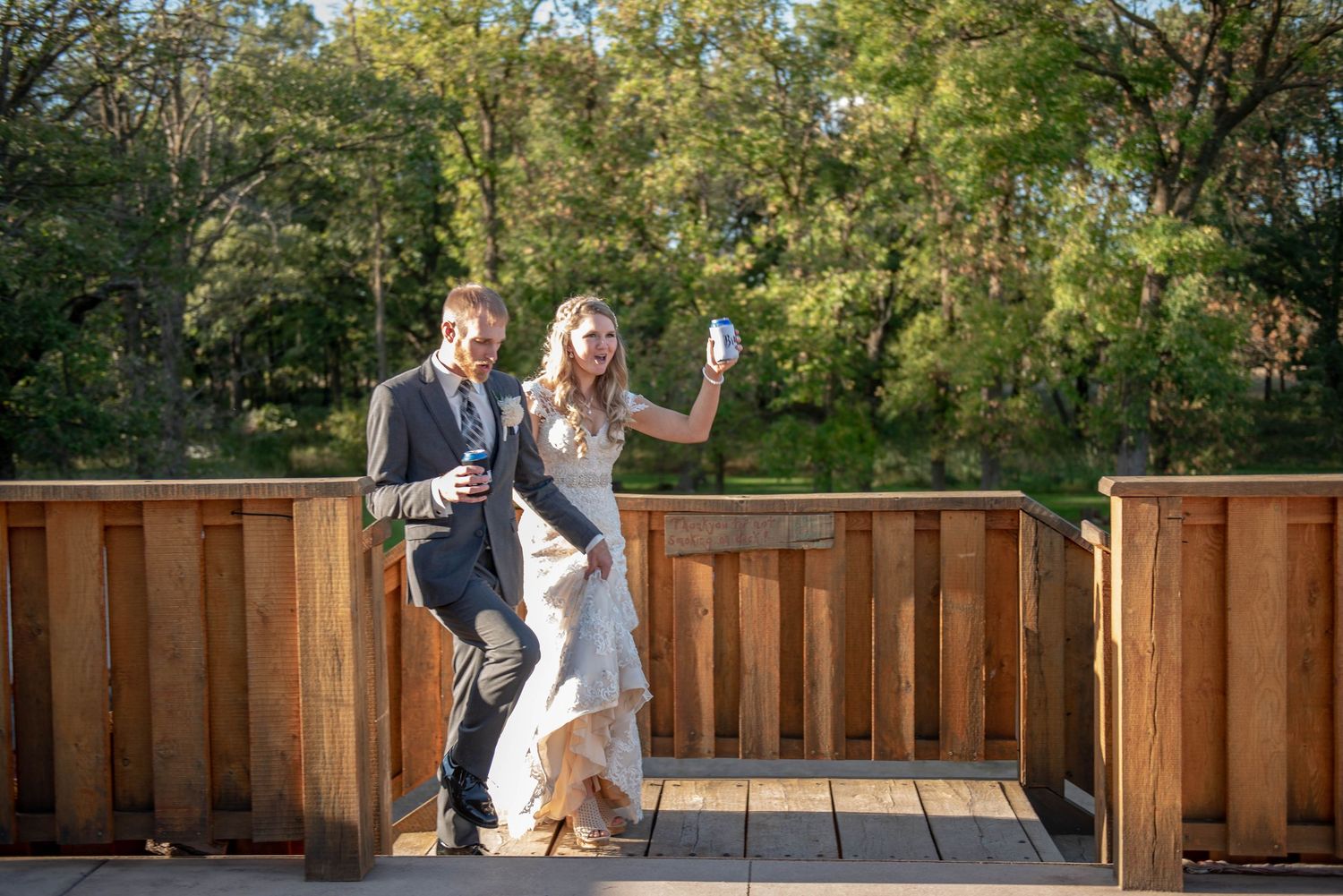 Couple stands on a wooden balcony deck surrounded by lush green trees during a wedding celebration. Rum River Barn Milaca Minnesota Weddings
