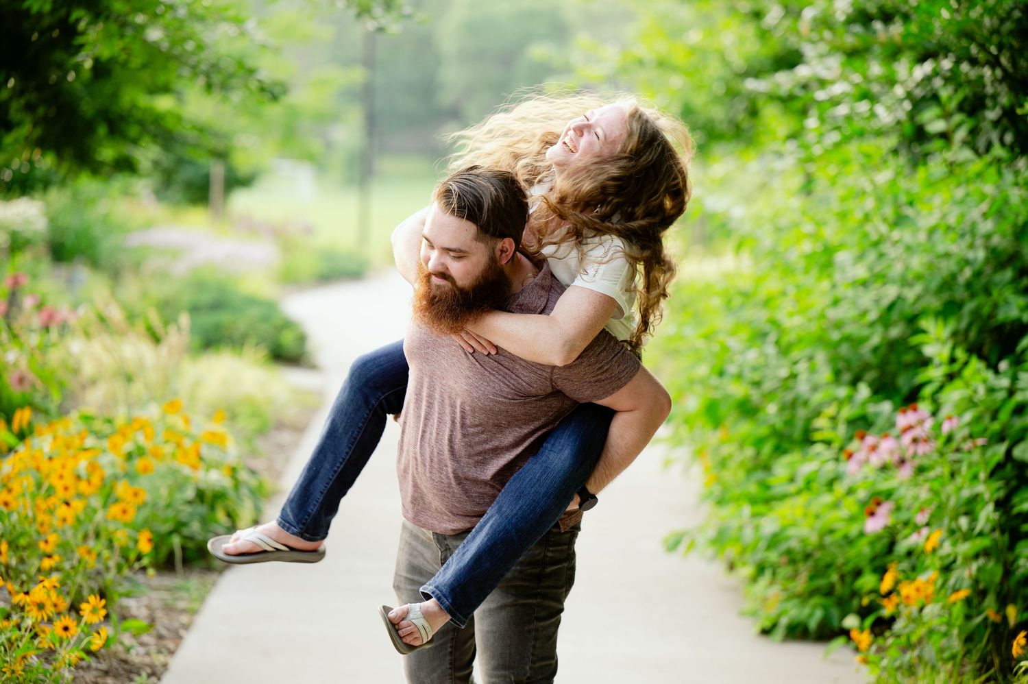 A couple sharing an intimate moment on a garden path surrounded by blooming flowers and foliage.