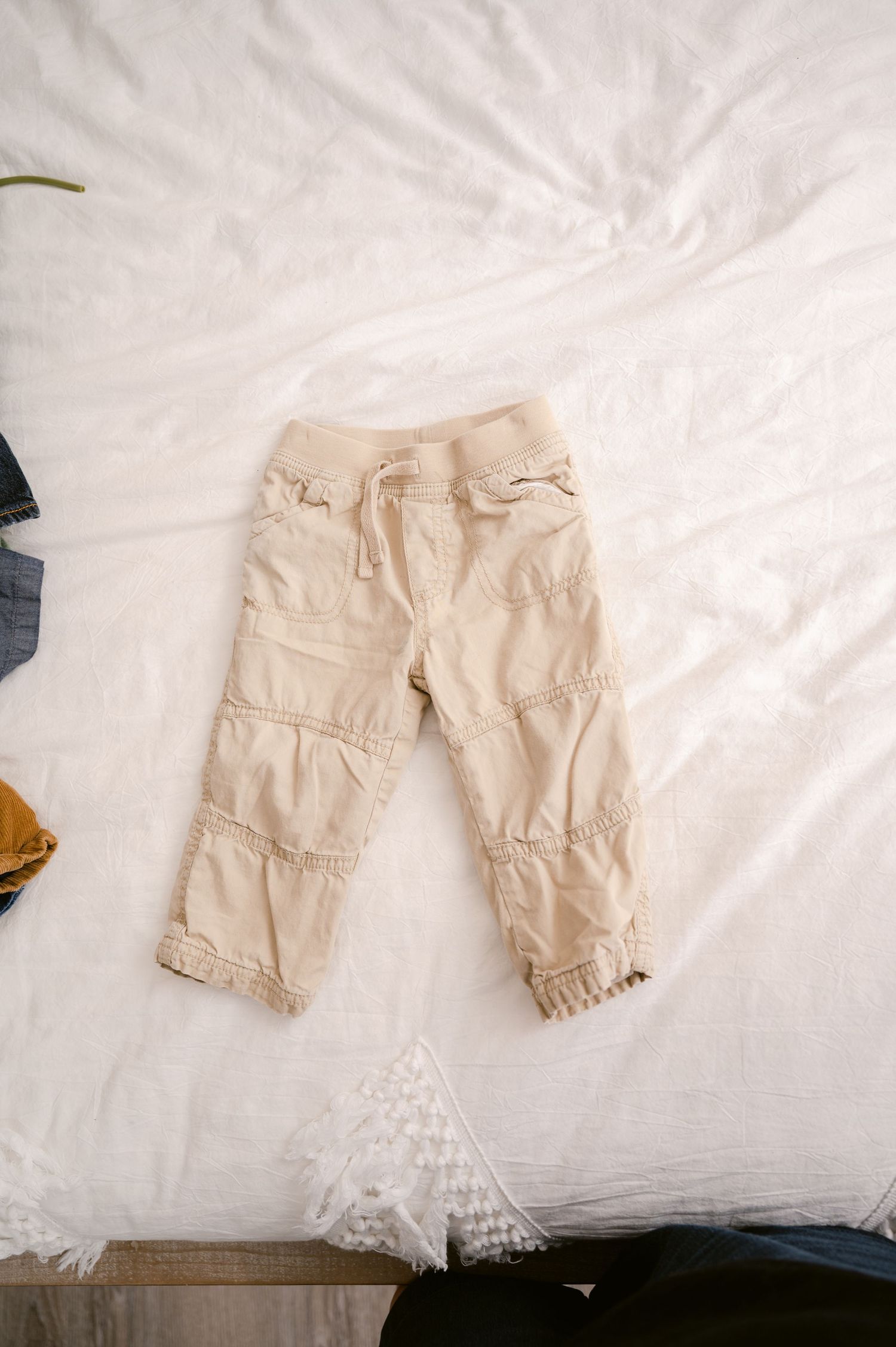 Beige cropped cargo pants with elastic cuffs laid flat on white bedding.