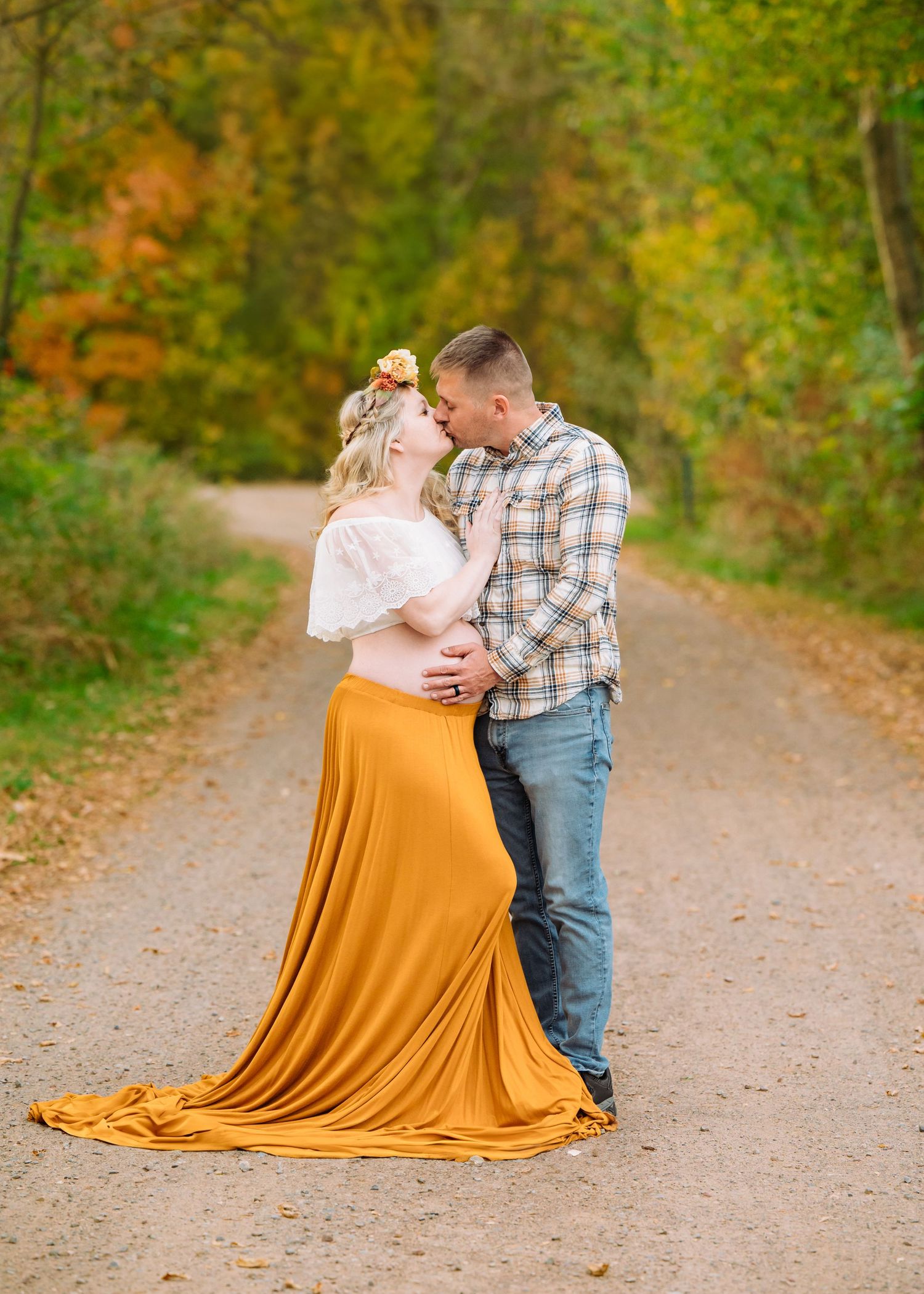 A couple shares an intimate moment on a fall path, with the woman wearing a flowing orange dress.