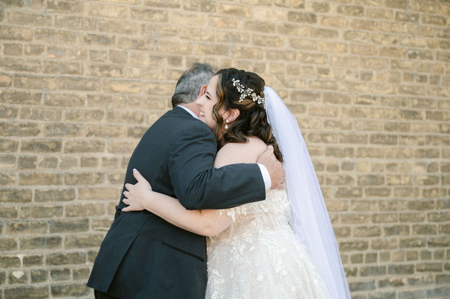 A heartfelt embrace between two people against a brick wall backdrop during a wedding celebration.