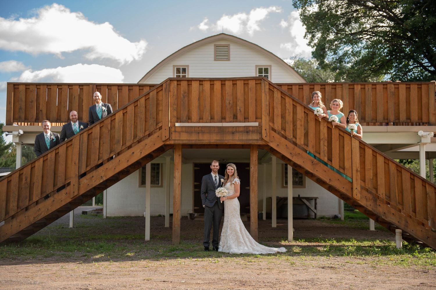Wedding party poses creatively on wooden stairs of a rustic barn venue. Rum River Barn Milaca Minnesota Weddings