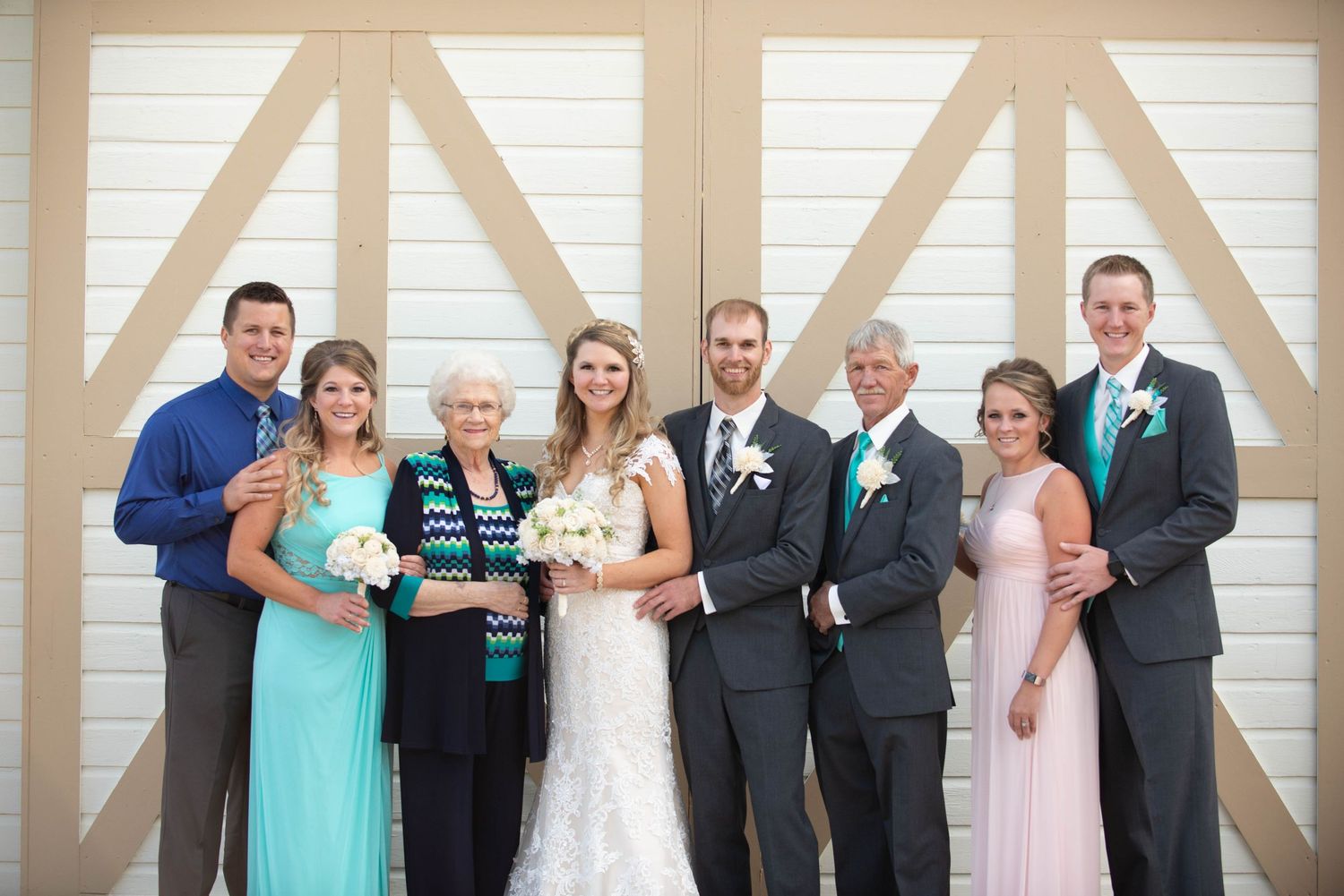 A wedding party poses together in formal attire against a light colored barn door background with teal accents. Milaca Minnesota Weddings