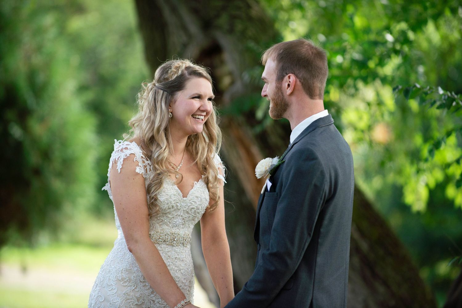 A couple shares a joyful moment together outdoors during their wedding day with green foliage in the background. Rum River Barn Milaca Minne