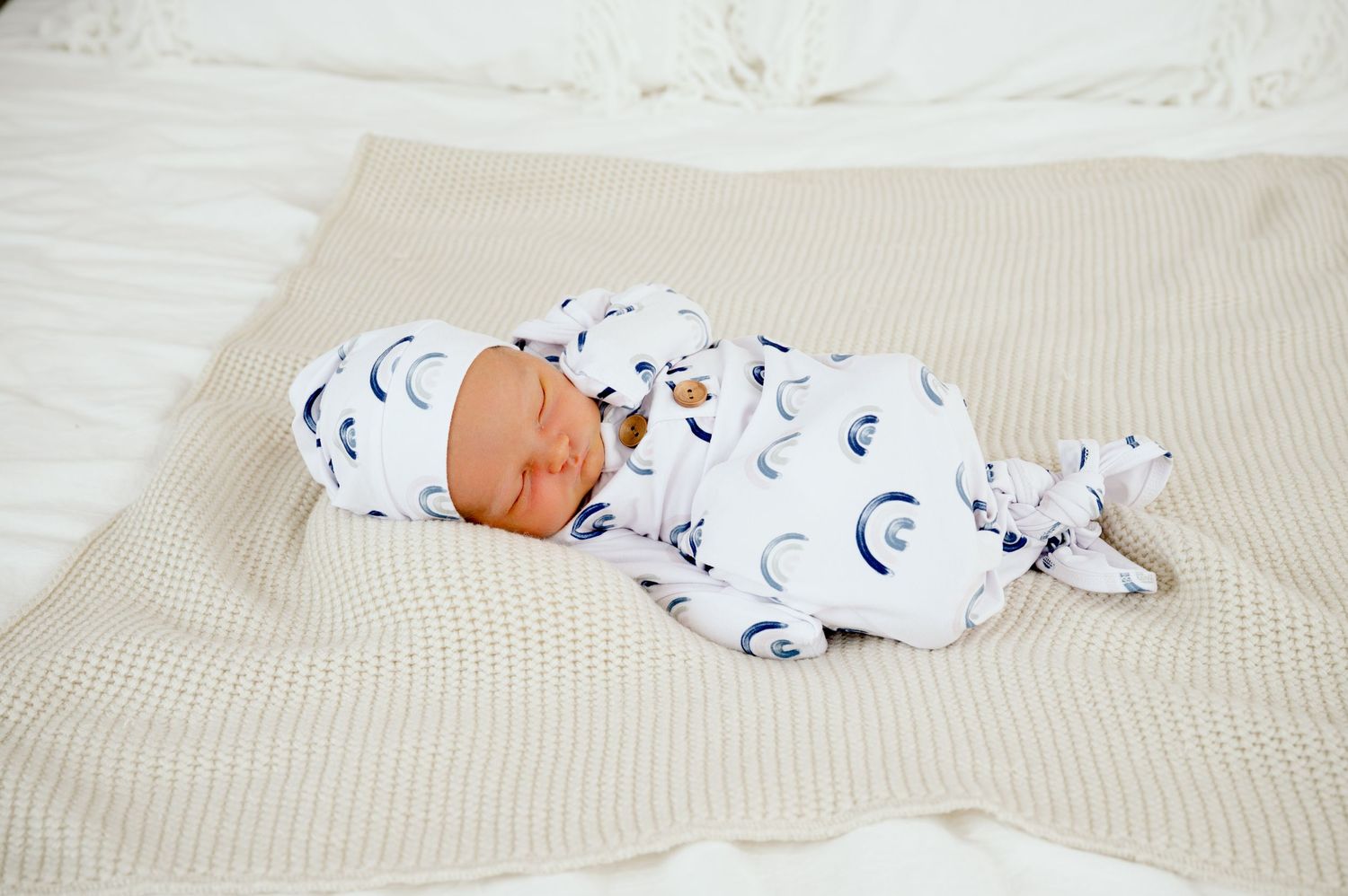 Newborn baby sleeps peacefully on beige blanket wearing white and blue patterned sleepsuit.