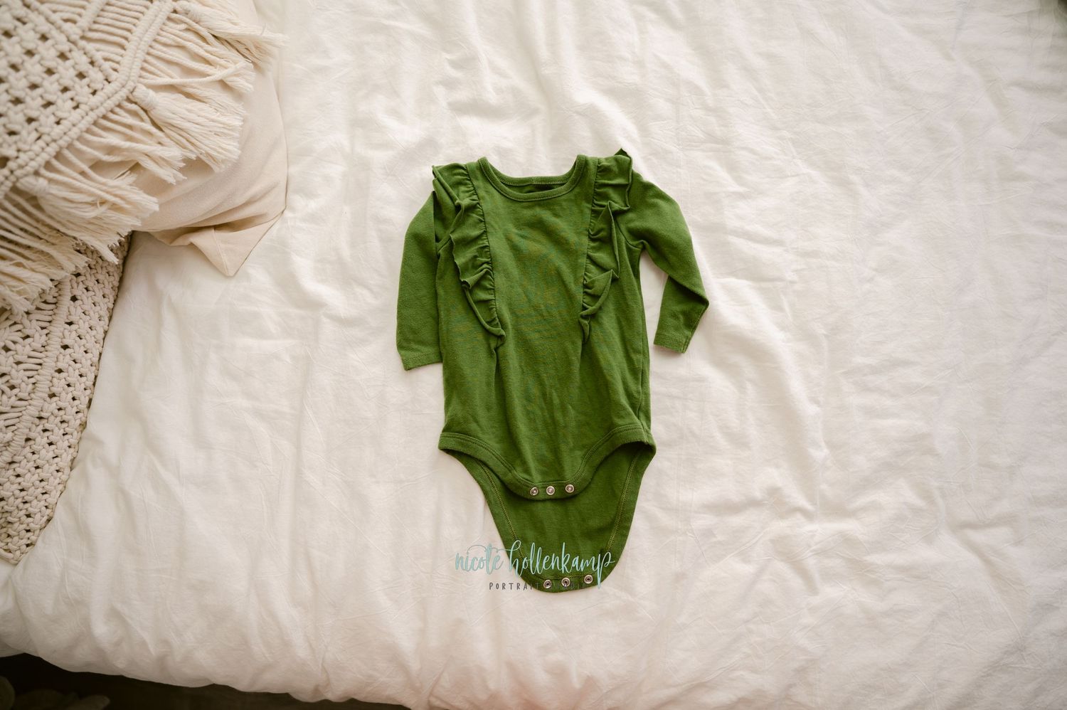 Green long-sleeved baby bodysuit with ruffle details laid on white bedding.