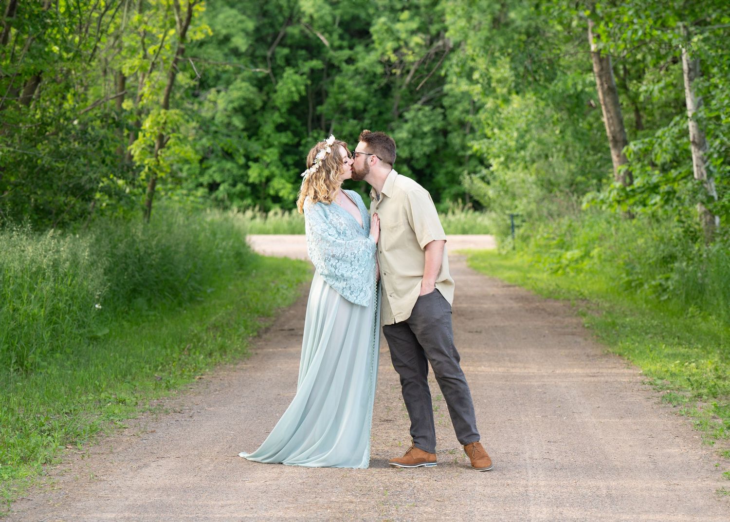 Romantic maternity photo of couple on tree-lined path.