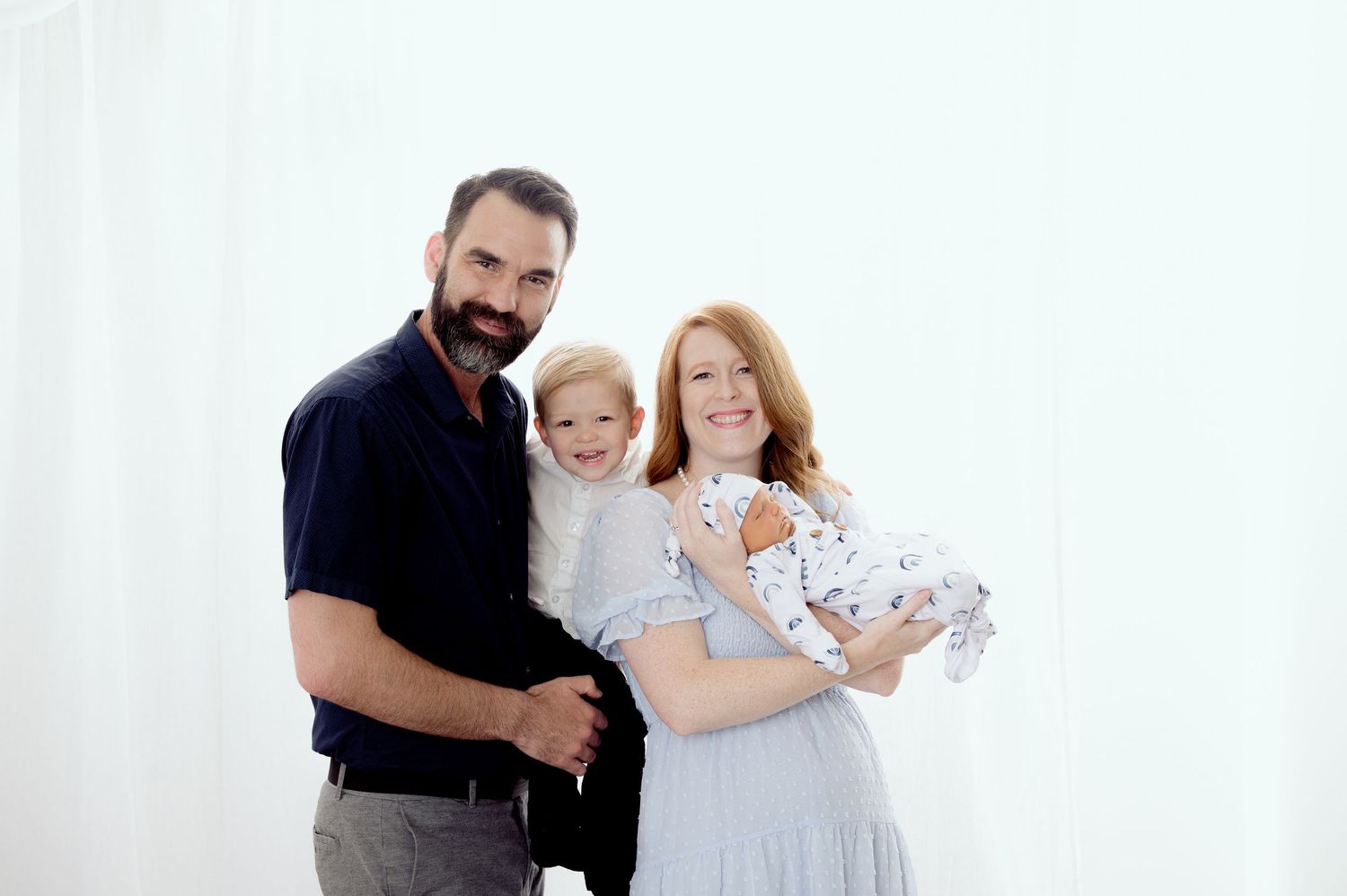 A family in coordinated navy and white outfits poses together against a light background during a portrait session.