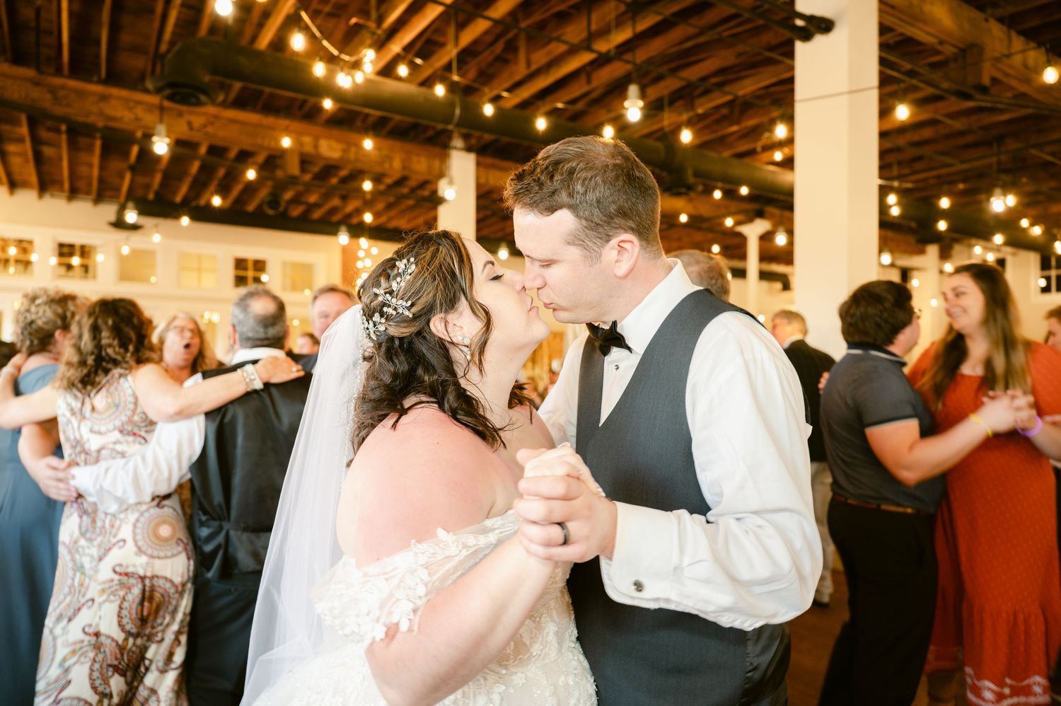 A couple dances surrounded by string lights at their wedding reception.