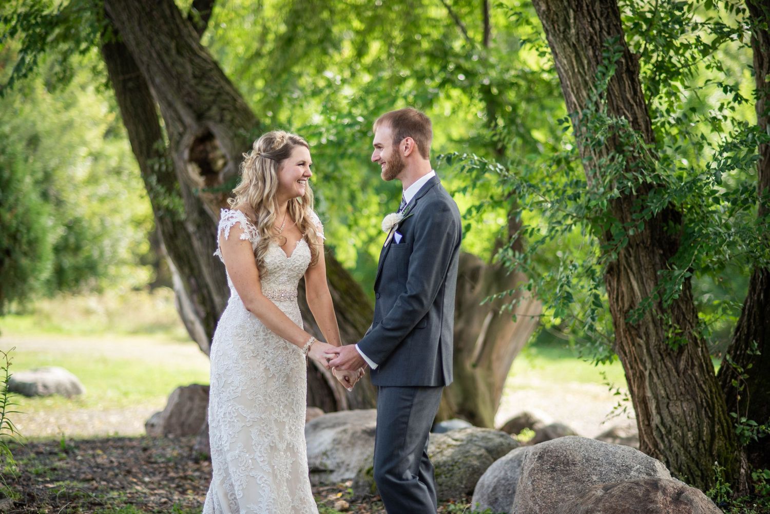 A bride in lace gown and groom in dark suit hold hands during their outdoor wedding ceremony.
