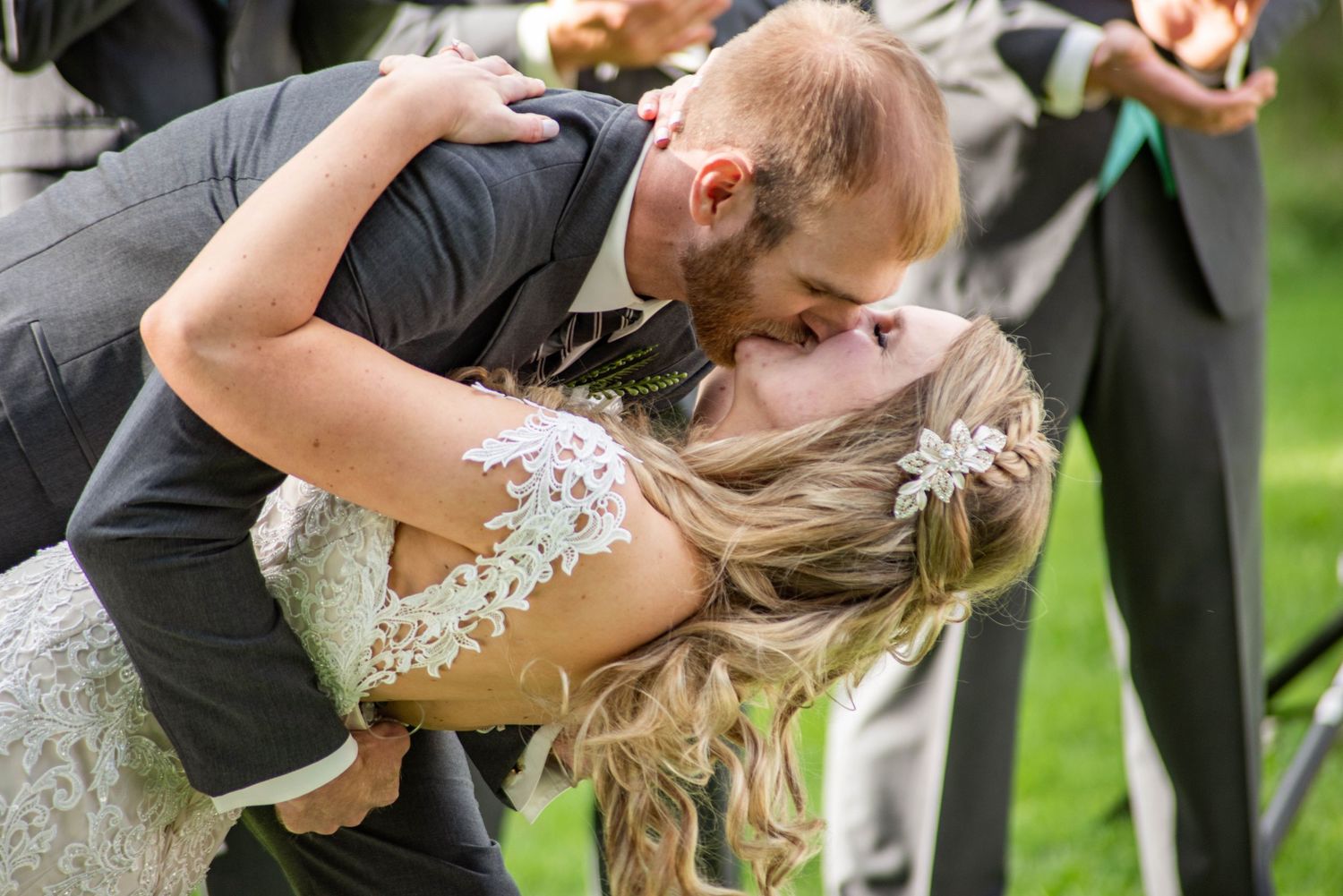A romantic dip kiss between newlyweds at an outdoor wedding celebration.
