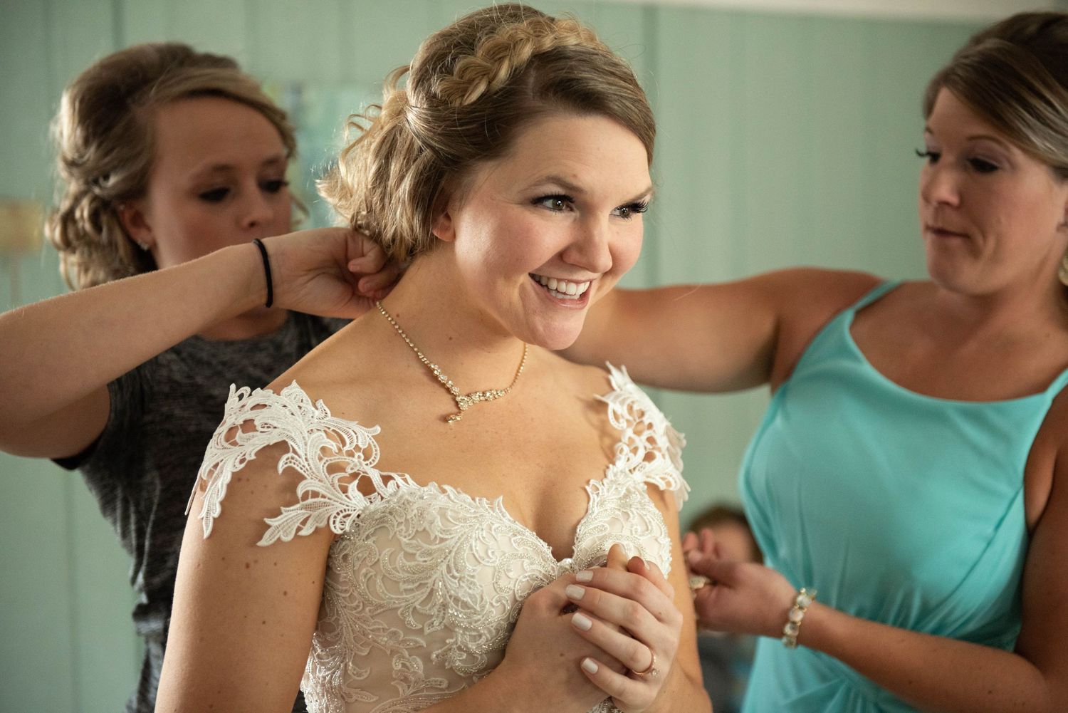 A wedding dress being fitted in a room with turquoise walls and attendants in matching dresses. Rum River Barn Milaca Minnesota Weddings