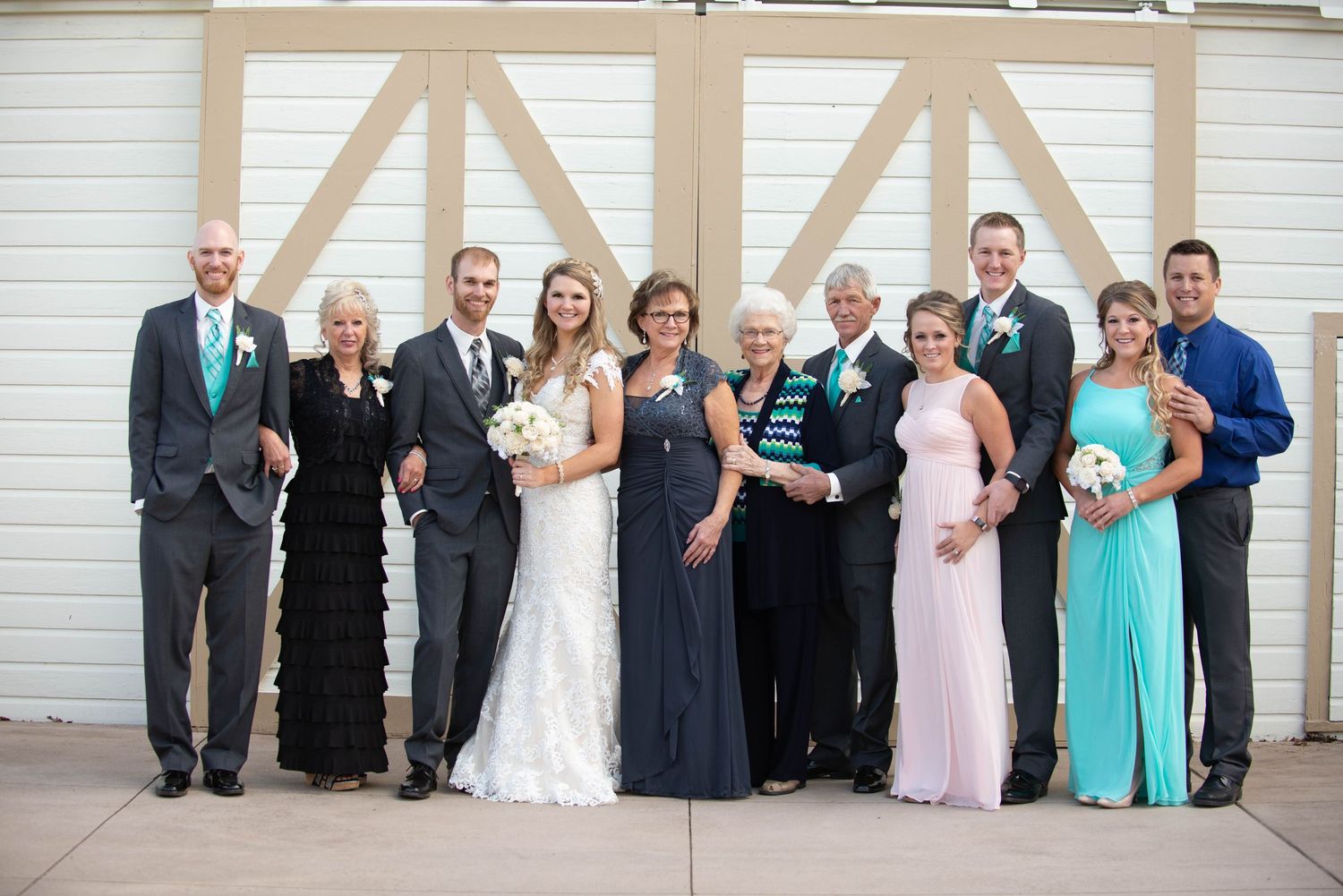 Wedding party in formal attire poses together against white barn doors for group portrait. Milaca Minnesota Weddings
