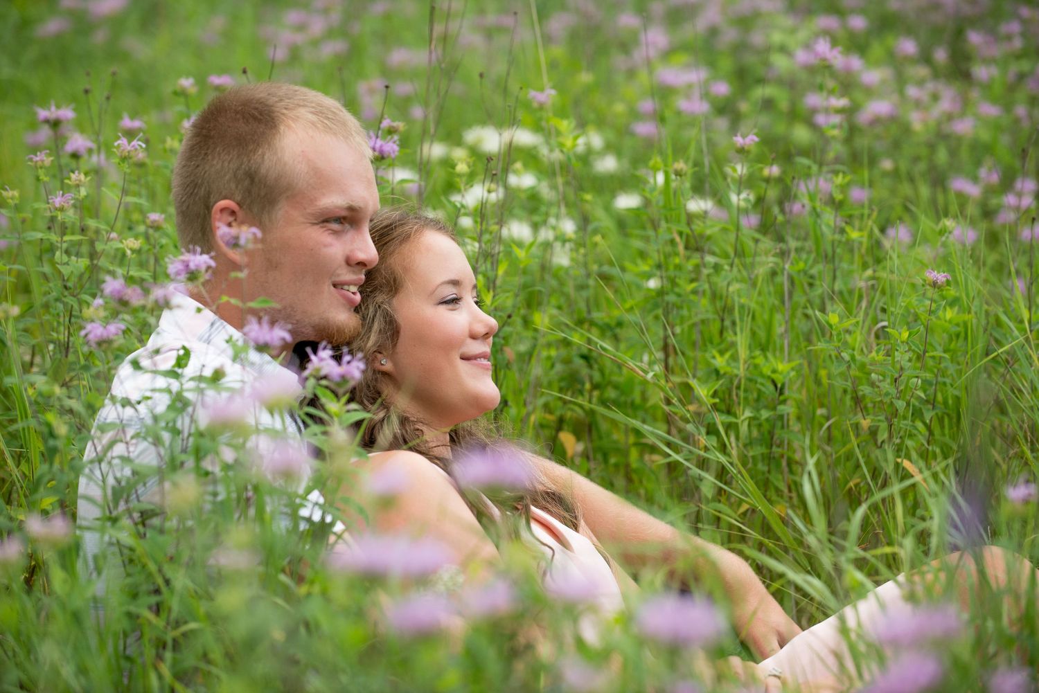 A couple lies in a field of wildflowers during a romantic summer photoshoot.