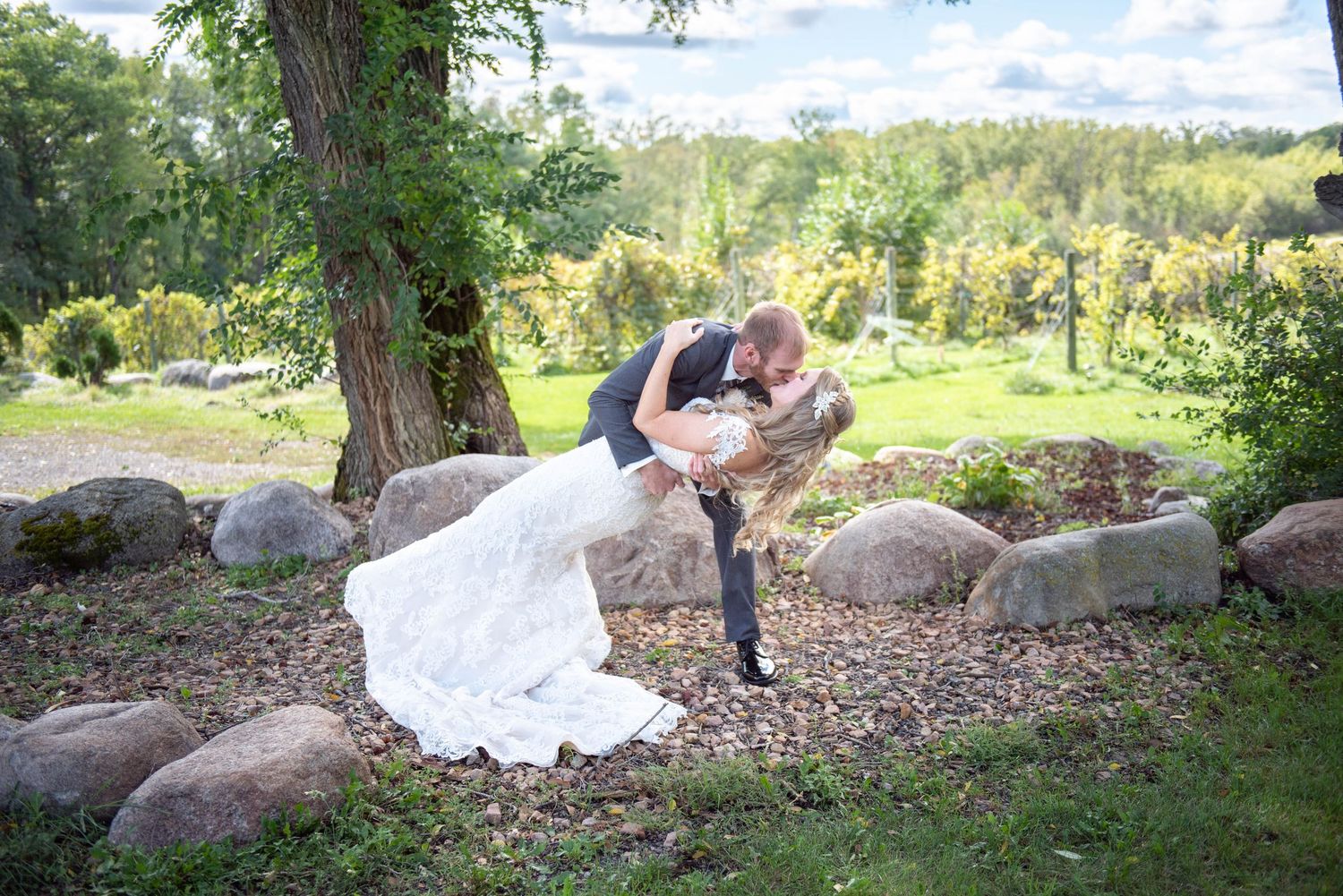 Couple in wedding attire posing for photos in scenic outdoor setting with large rocks and trees. Rum River Barn Milaca Minnesota Weddings