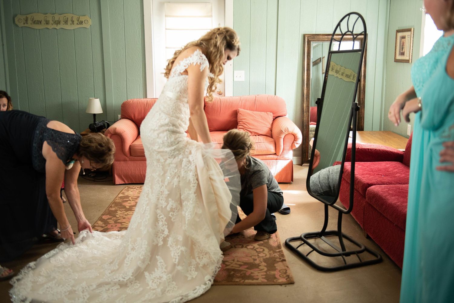 A white lace wedding dress being fitted in a room with red couches. Rum River Barn Milaca Minnesota Weddings