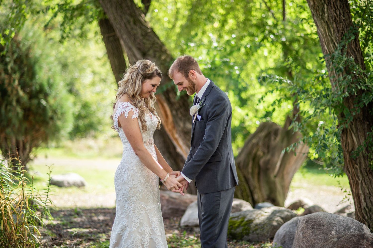 A wedding couple holds hands and shares a romantic moment in a sunlit garden setting.