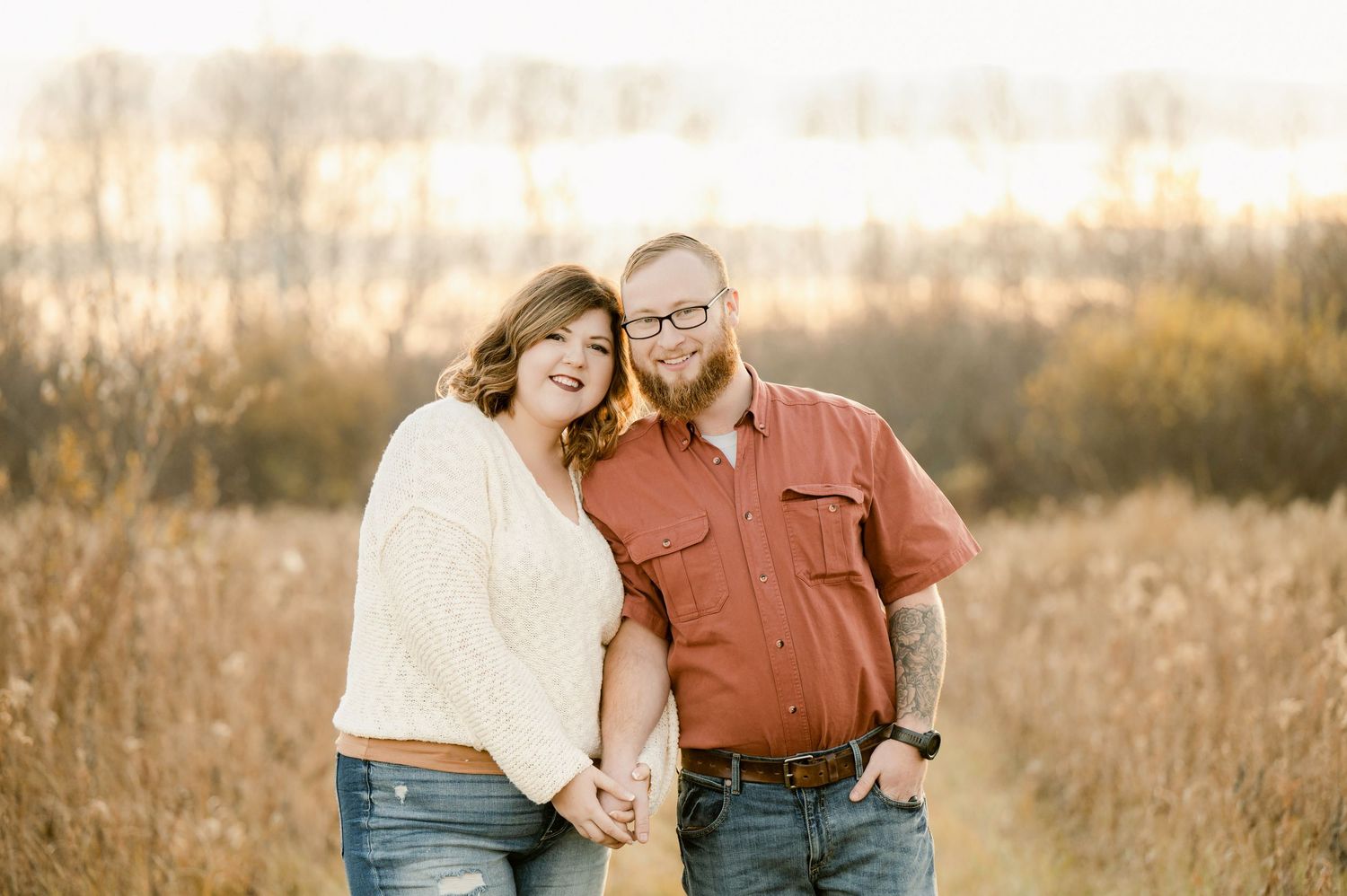A couple embraces in a sun-drenched meadow with tall golden grass during sunset, creating a warm romantic moment.