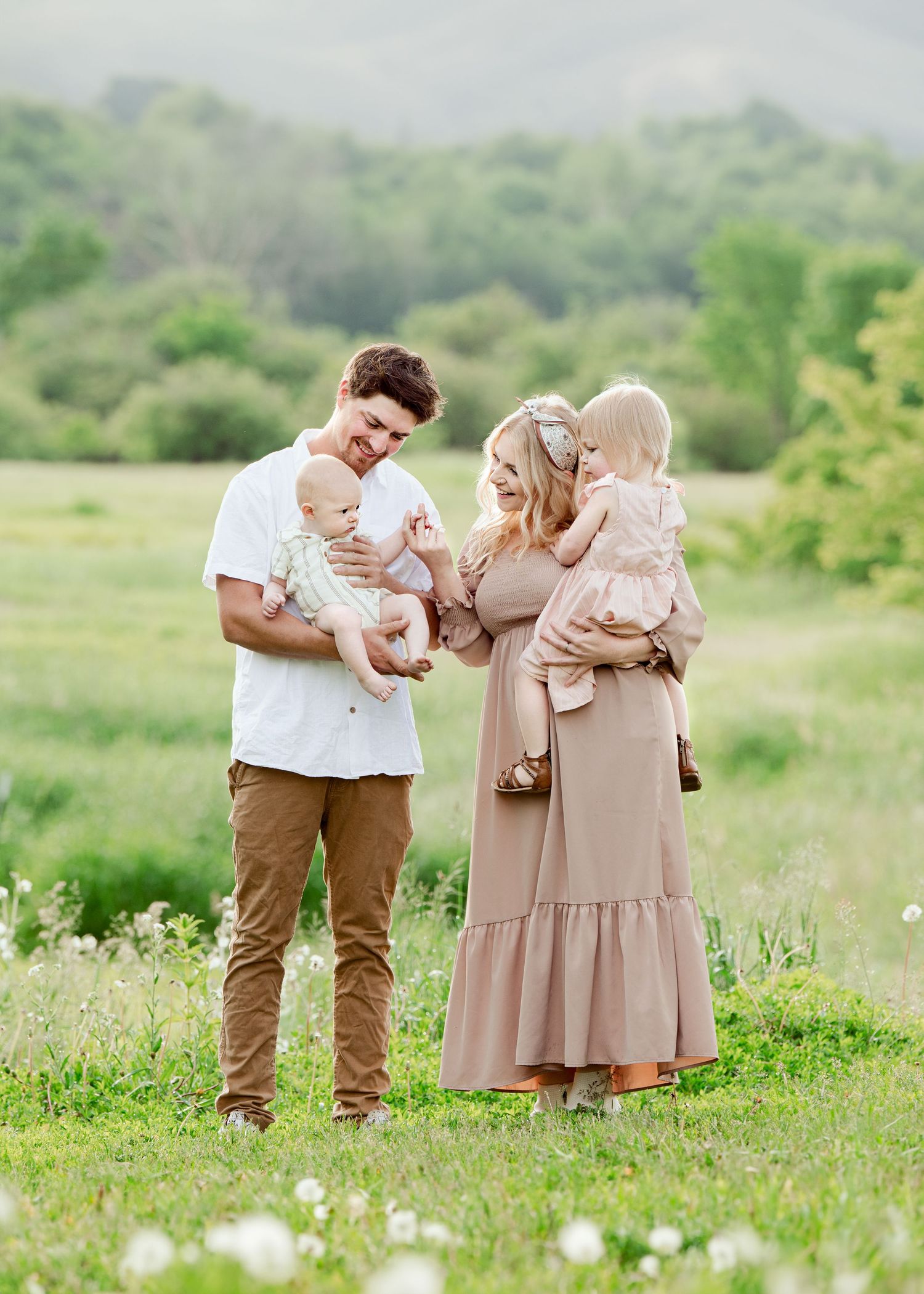 Family enjoying a tender moment together in a sunny meadow with mountains in the background.