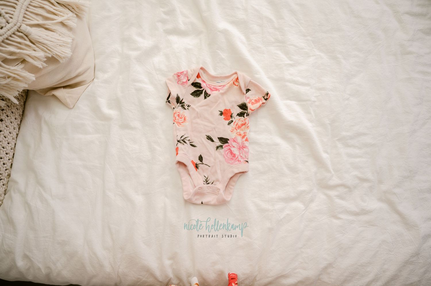Pink floral baby onesie lying on white bedding with soft knit fabric visible in corner.