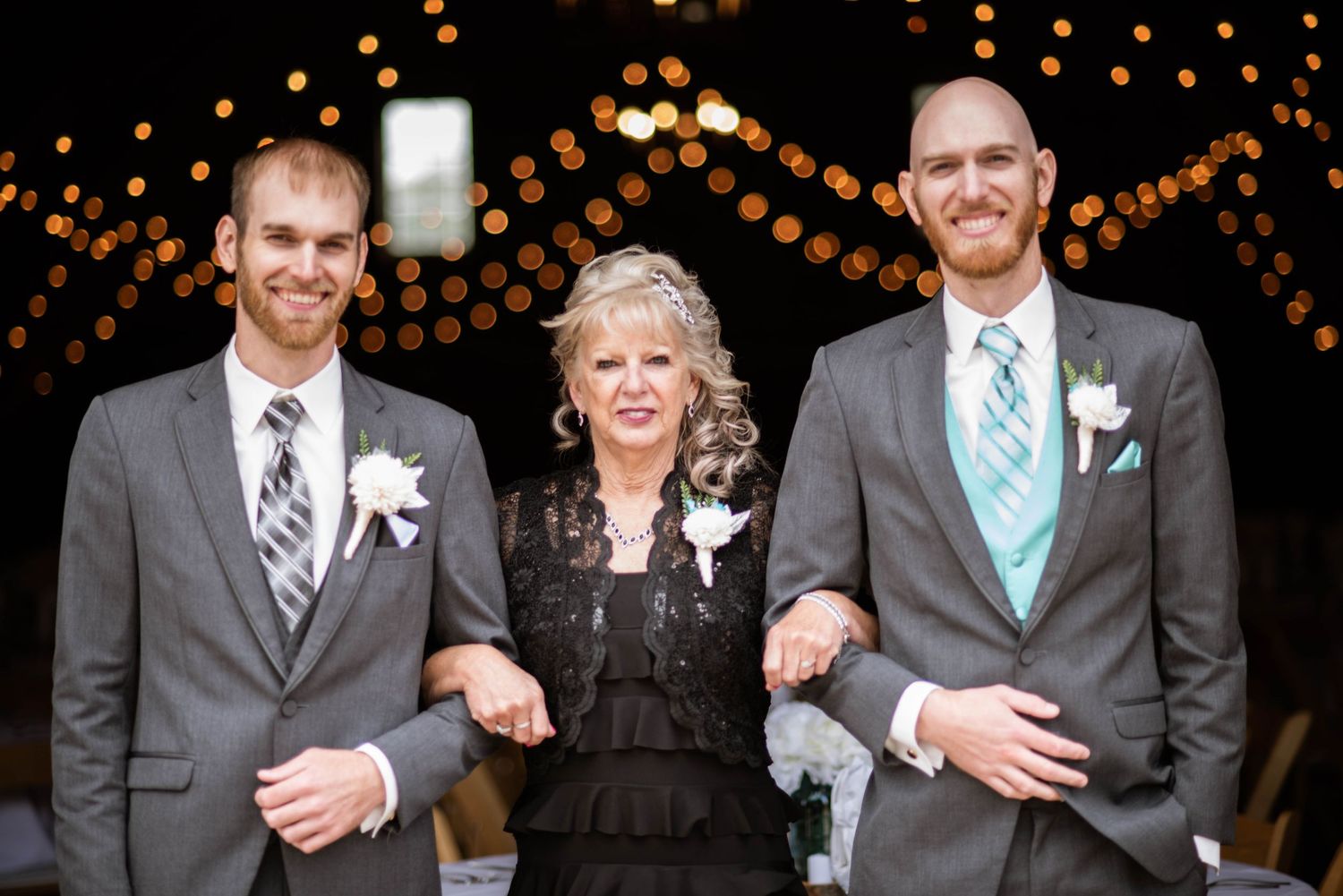 Three people in formal attire pose together with twinkle lights in the background at an elegant event.