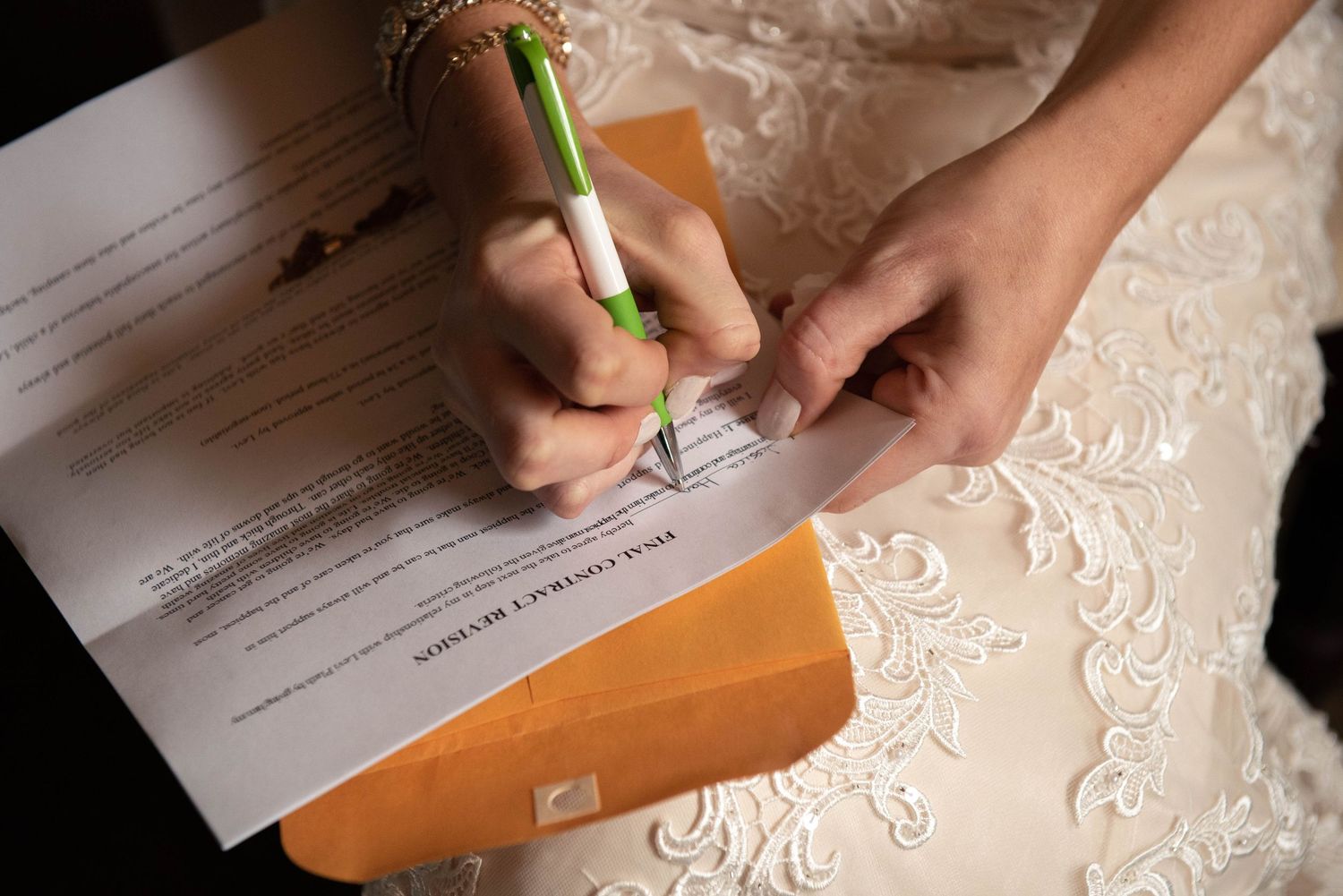 Close-up of hands signing wedding documents with a green pen on a rustic wooden surface. Rum River Barn Milaca Minnesota Weddings