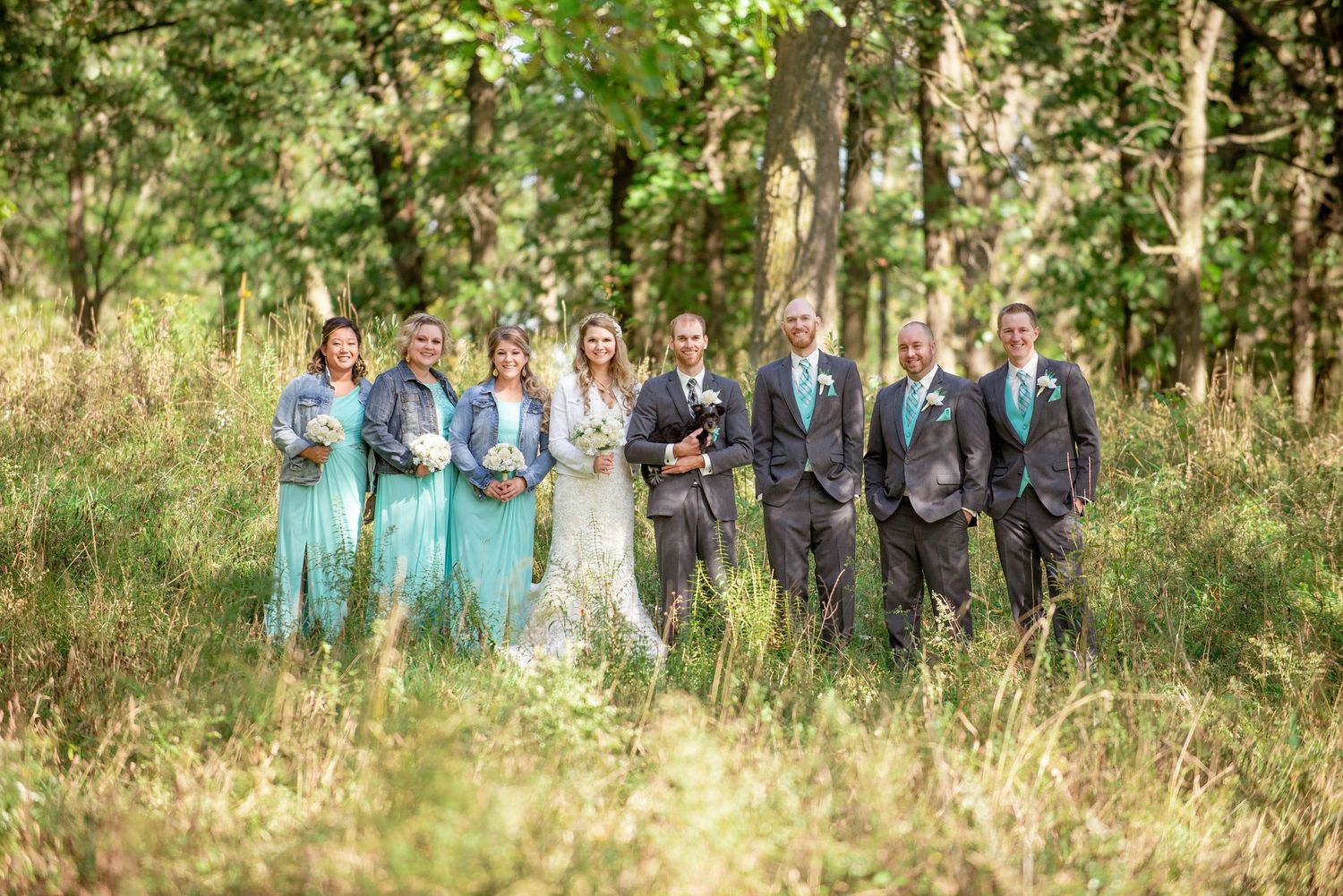 A wedding party poses in coordinated turquoise and grey attire against a natural outdoor backdrop. Rum River Barn Milaca Minnesota Weddings
