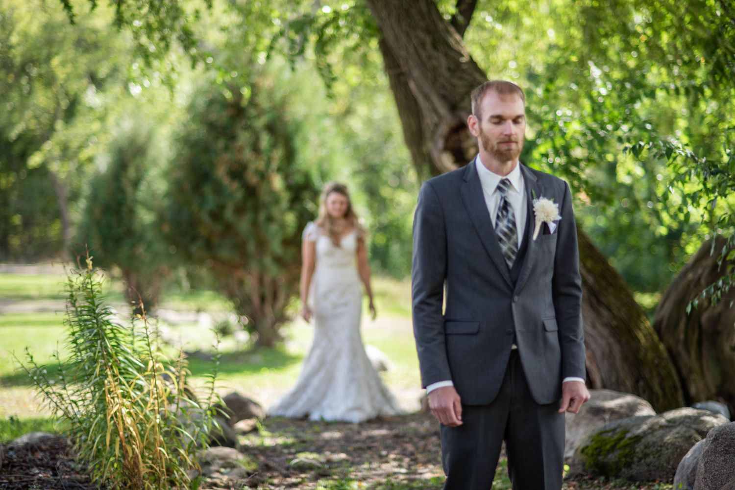 Wedding party poses for portraits in a lush green garden setting on a sunny summer day.
