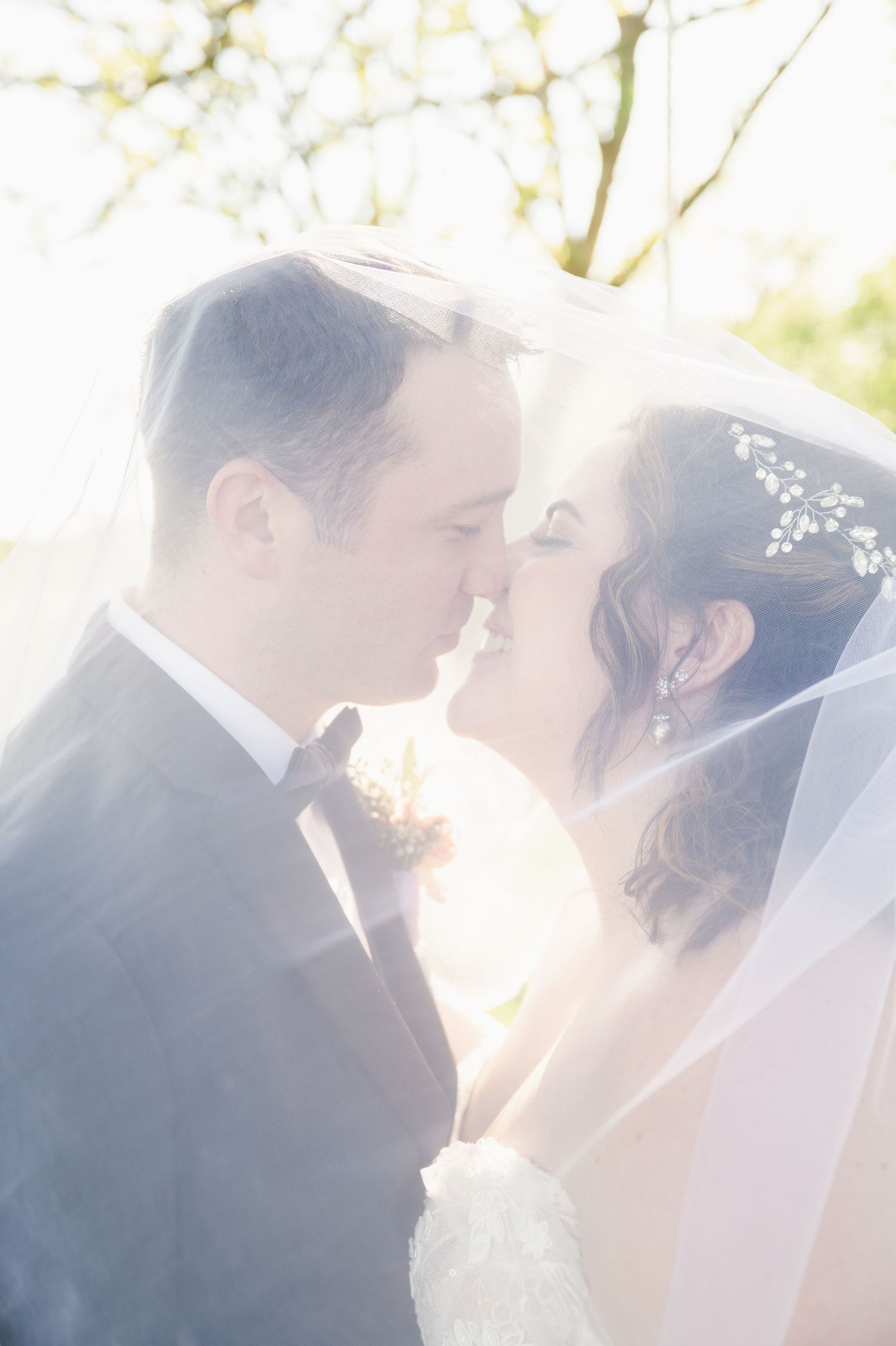 Romantic newlyweds share an intimate moment in soft sunlit garden setting during wedding celebration.
