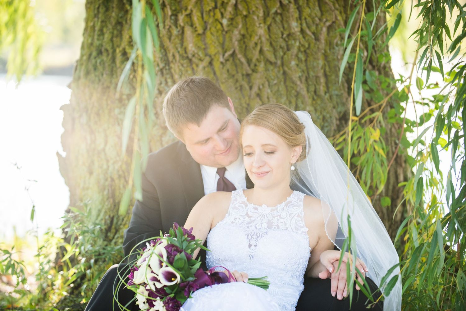 Romantic wedding couple poses under willow tree branches on sunny afternoon. Andover wedding at Magestic Oaks Golf Club
