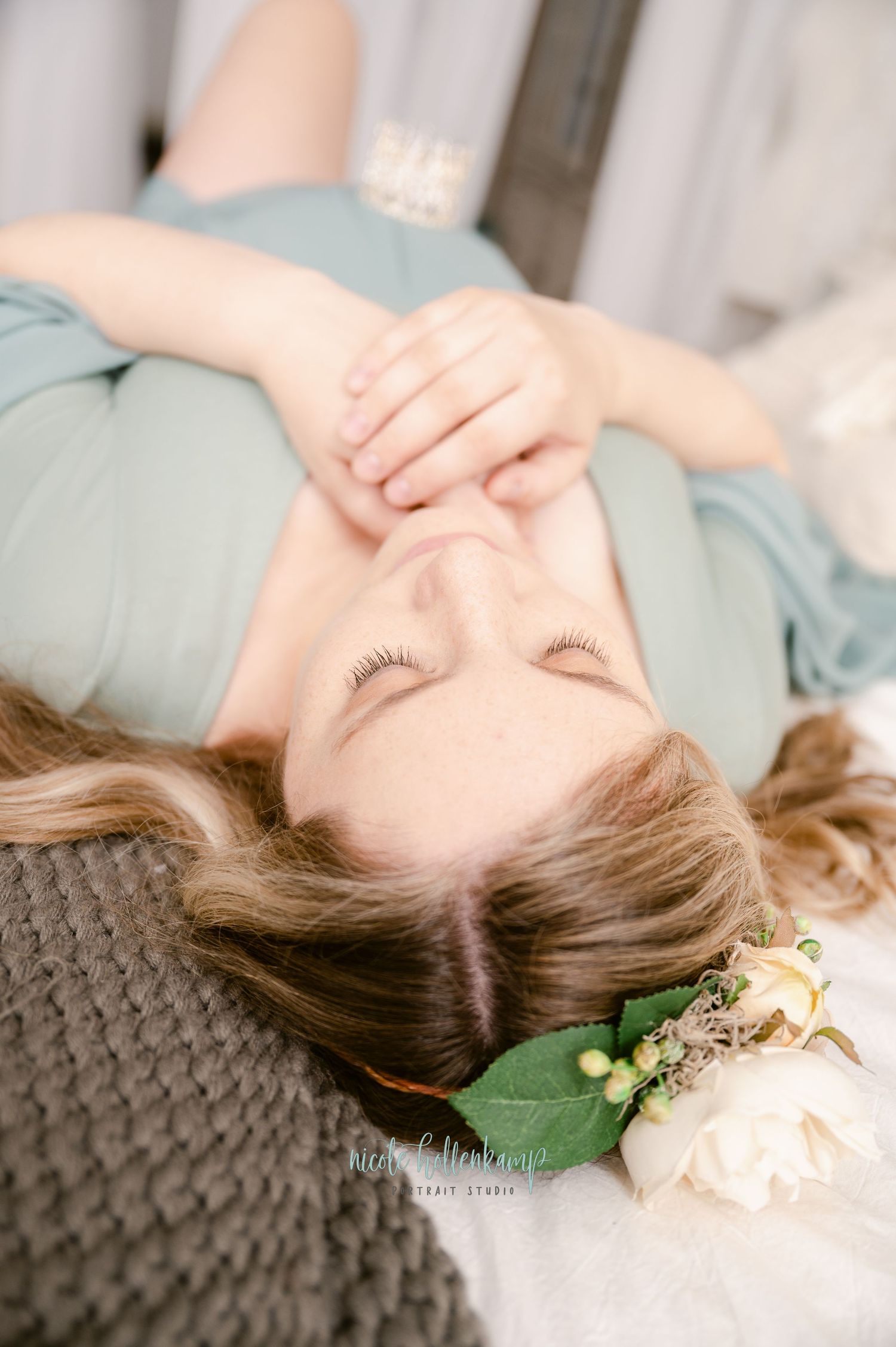 Ethereal boudoir portrait shows a person in blue reclining on grey textured bedding with white roses beside them.