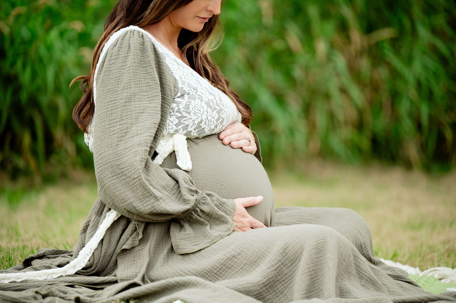 Side view of pregnant woman in grey dress cradling baby bump during outdoor maternity photoshoot.