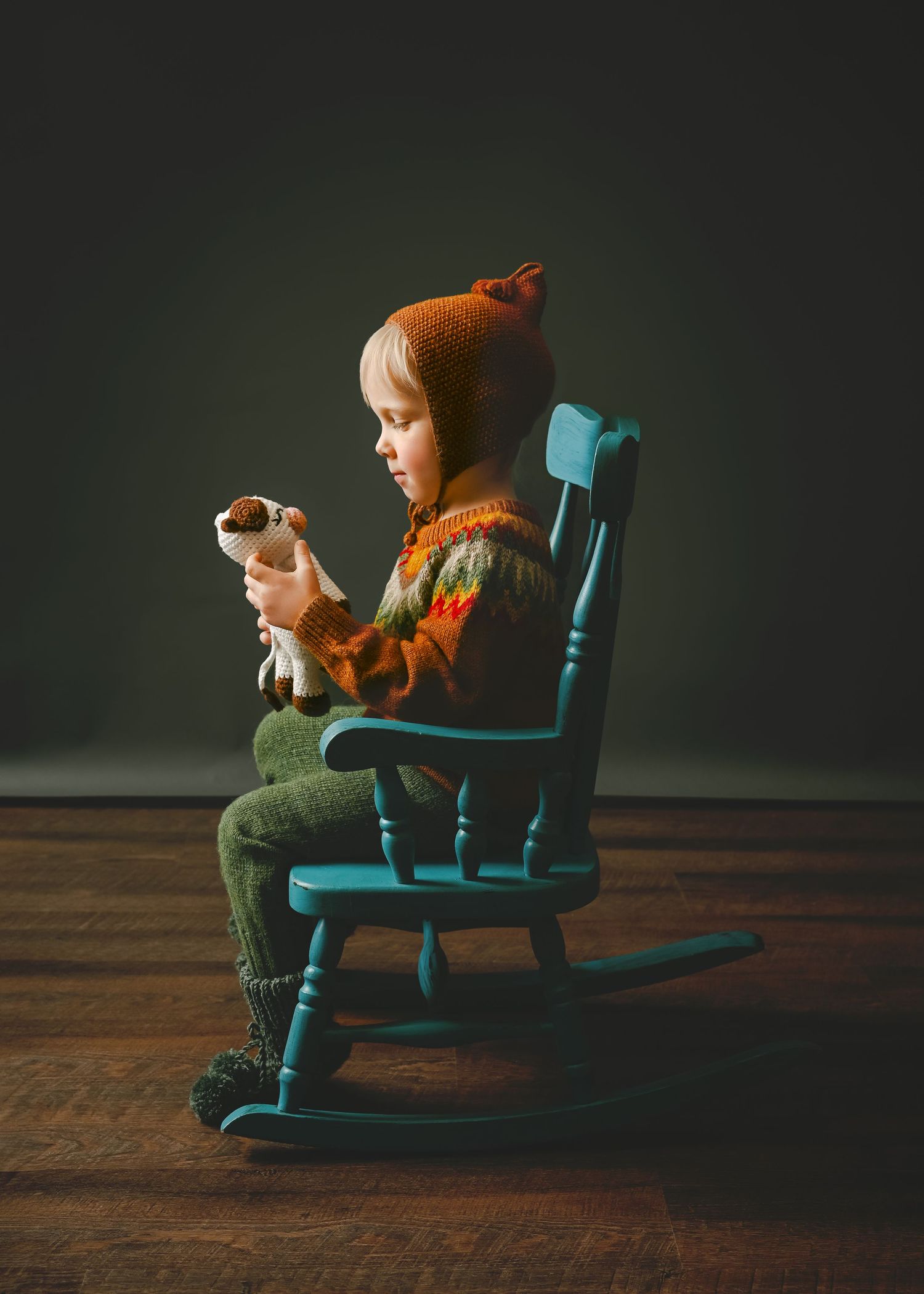 Child in orange sweater sits sideways on blue rocking chair holding a toy.