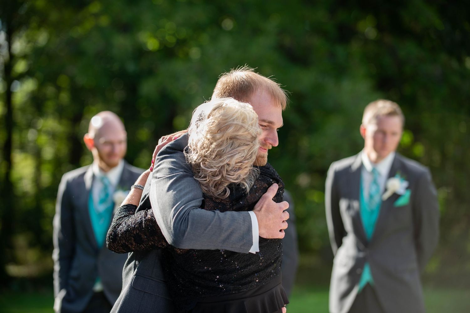 Emotional embrace shared between wedding guests during outdoor ceremony with teal accents. Rum River Barn Milaca Minnesota Weddings