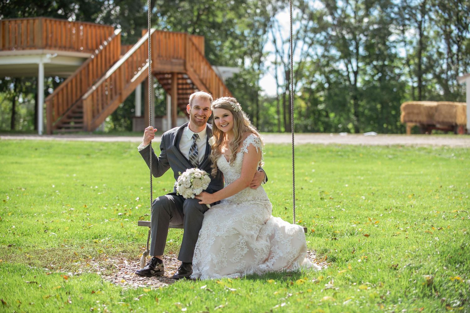 Couple sits on a swing in a grassy field on their wedding day. Rum River Barn Milaca Minnesota Weddings